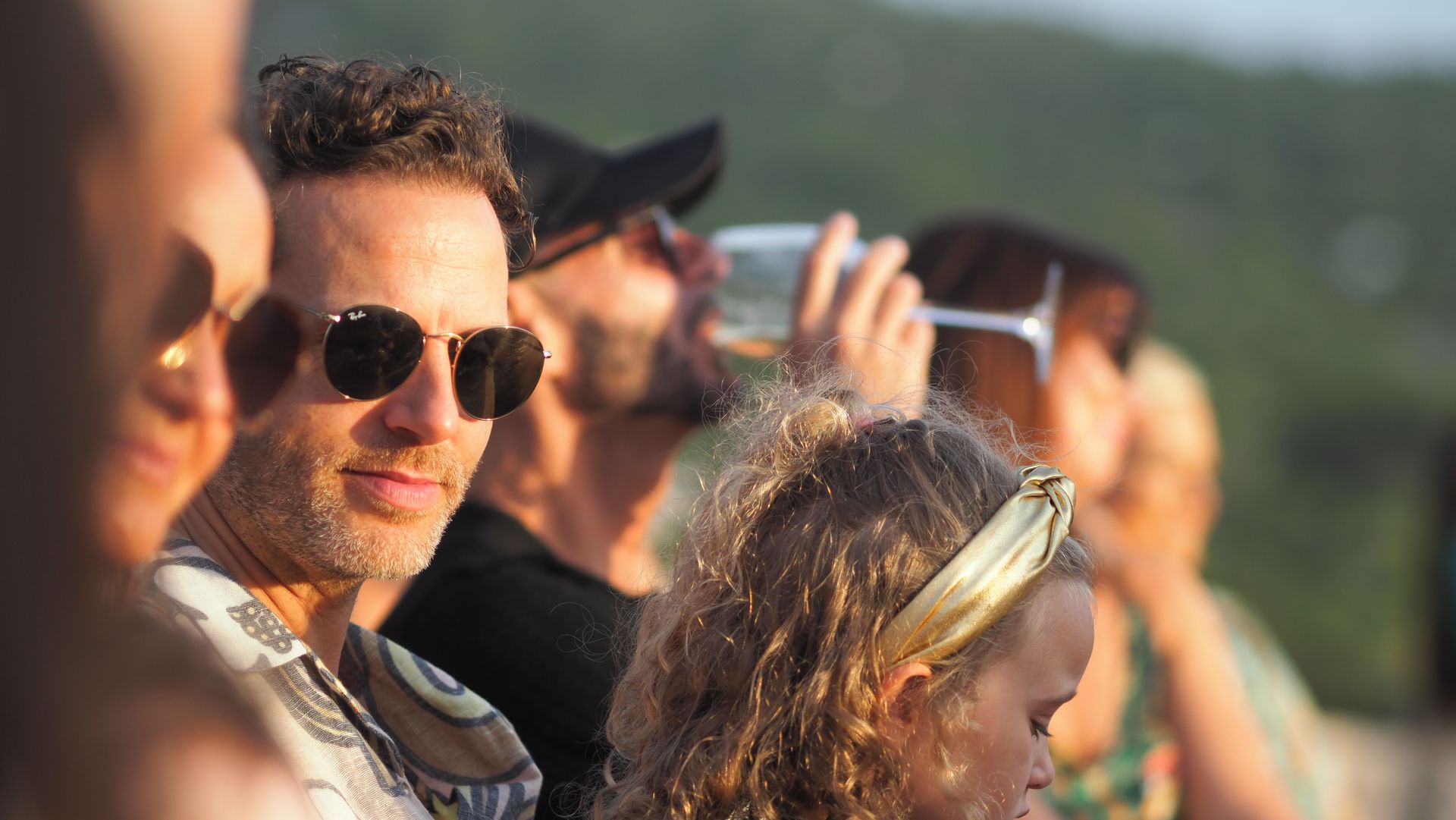 People wearing sunglasses watching an outdoor event in bright sunlight