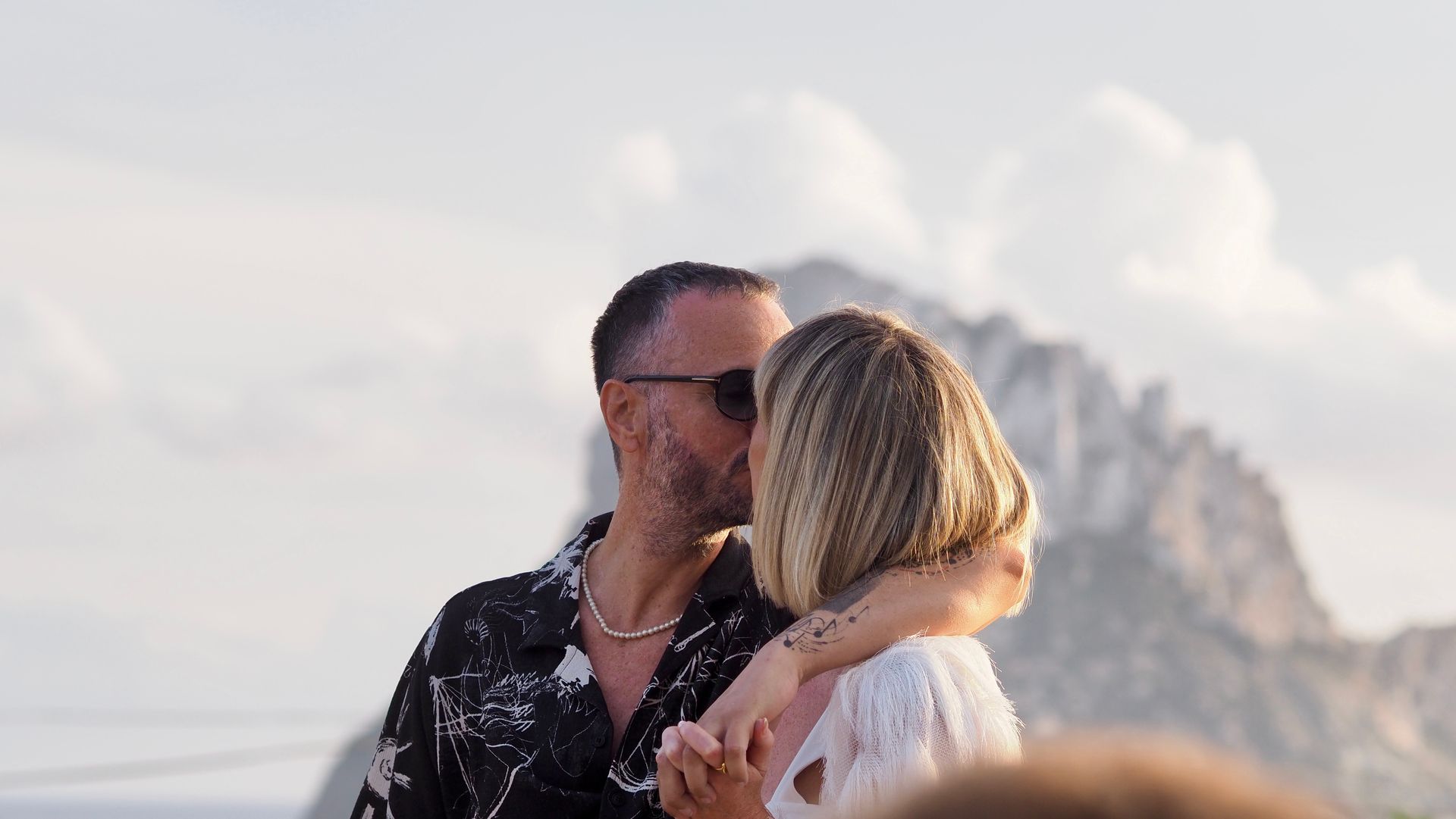 Couple kissing by the sea with cliffs in the background at sunset
