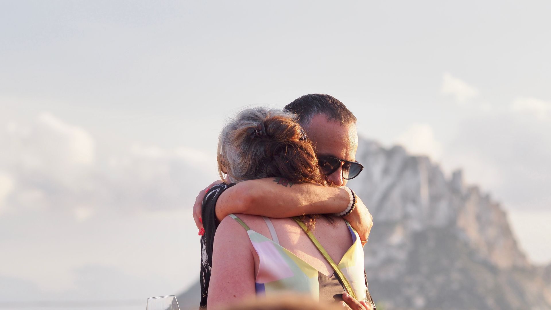 Two people hugging outdoors with rocky mountains in the background at sunset
