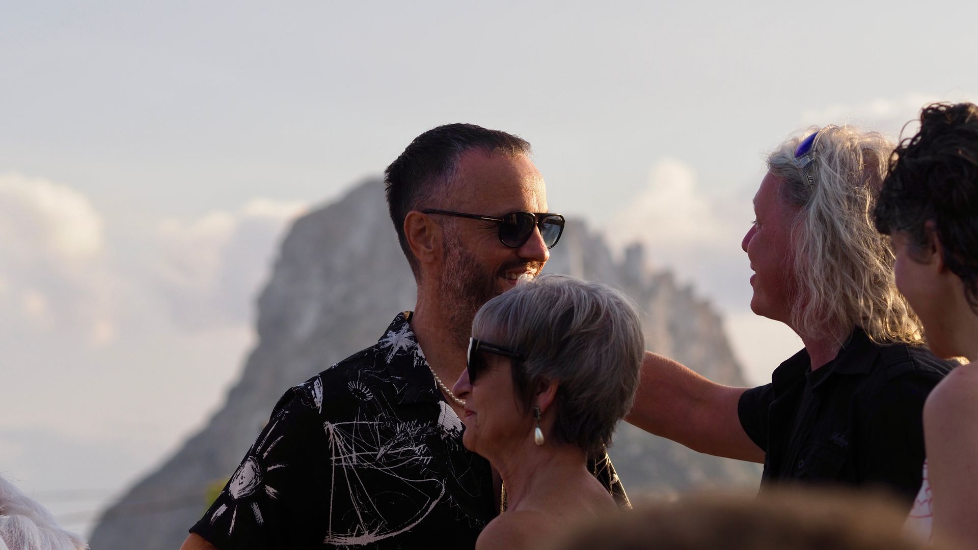 People chatting outdoors at sunset with rocky cliffs in the background