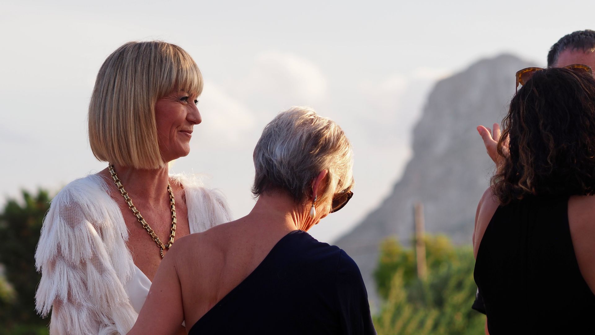 Three people outdoors at sunset, chatting with mountains in the background.