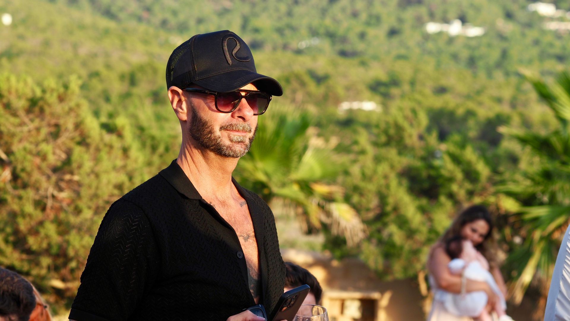 Man in black cap and sunglasses outdoors with green hills in the background