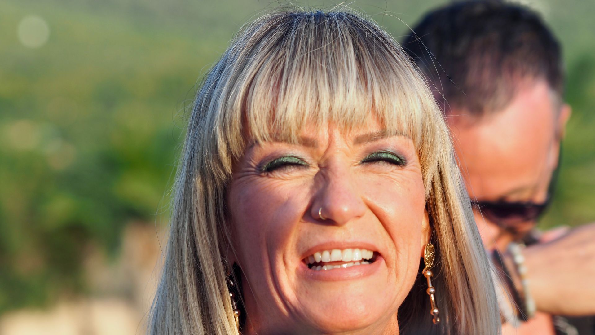 Smiling blonde woman outdoors with a blurred person in the background