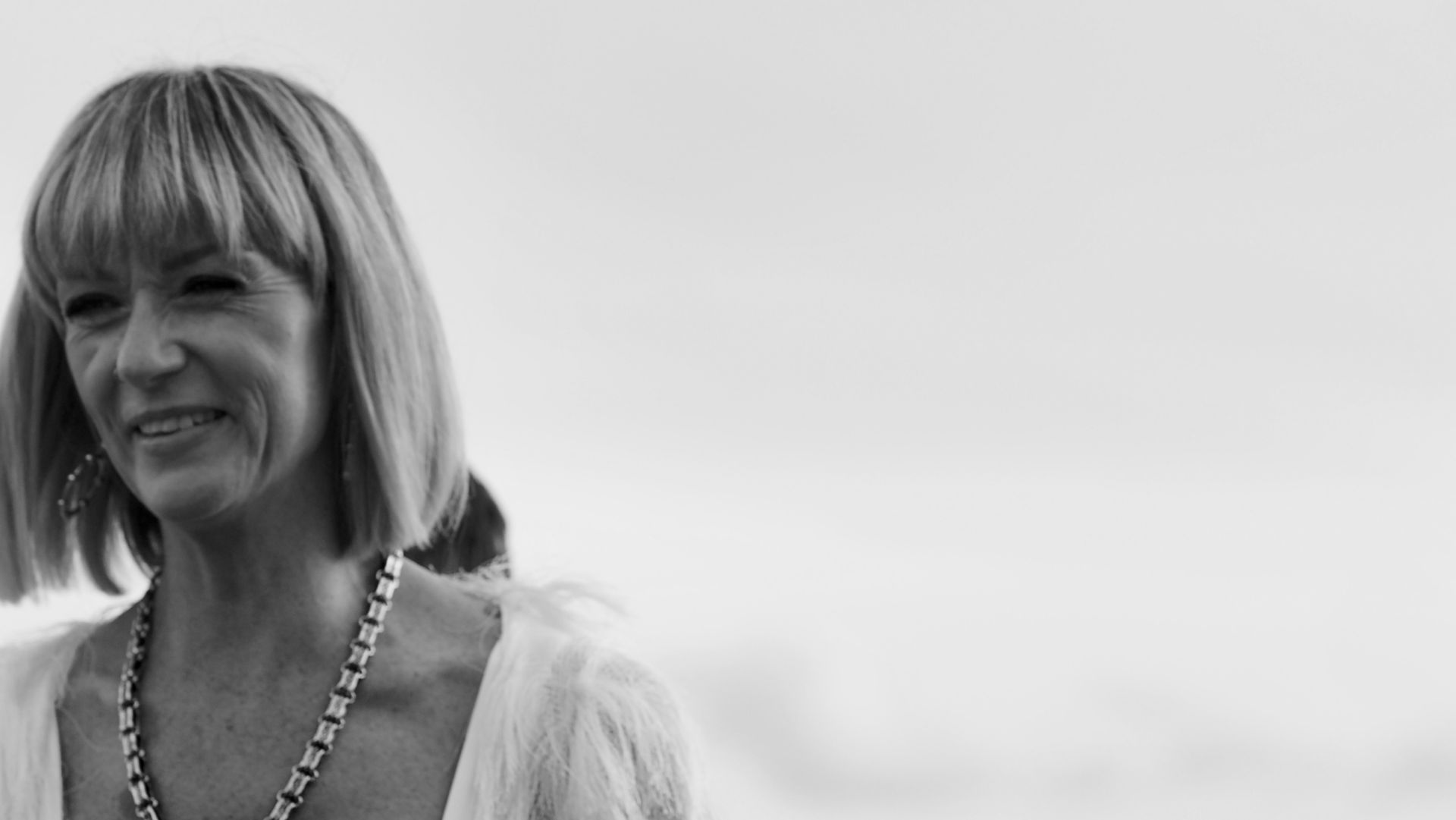 Smiling woman in a light dress standing outdoors against a bright sky
