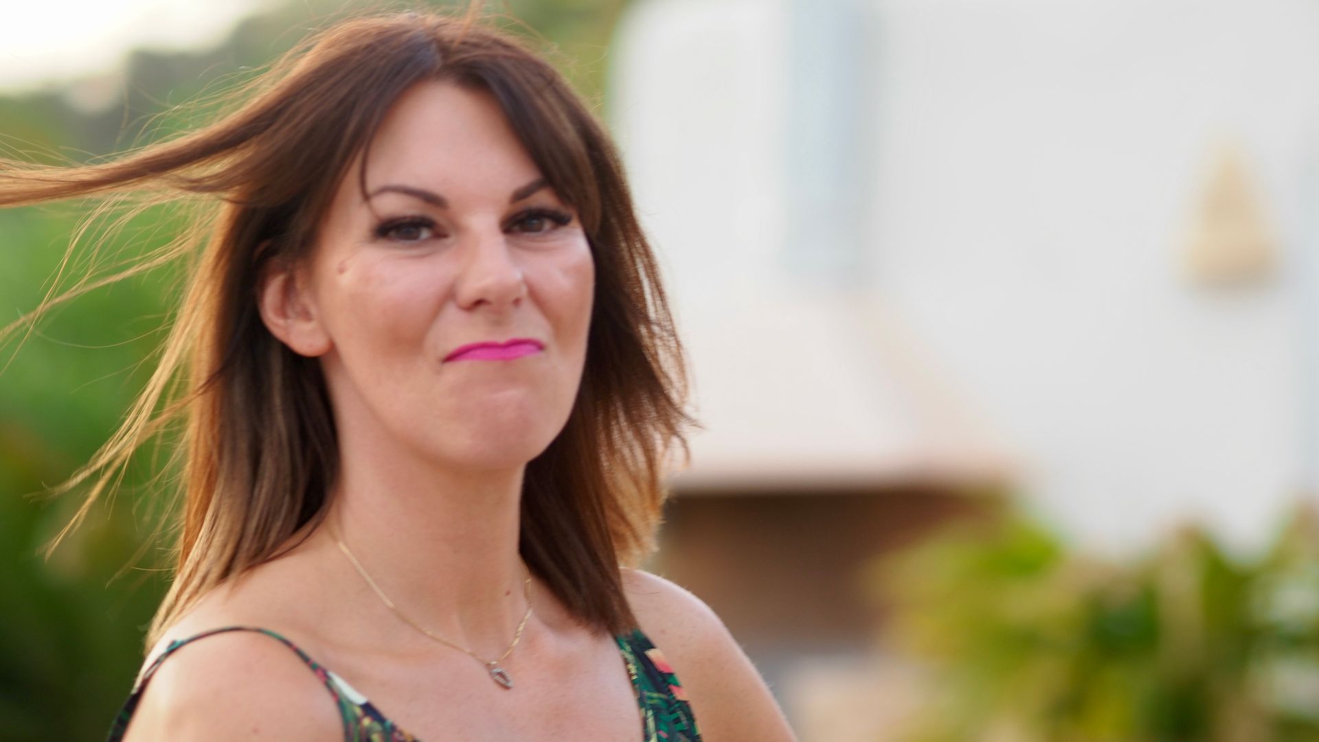 Woman outdoors with shoulder-length brown hair, wearing a green patterned top and a slight smile.