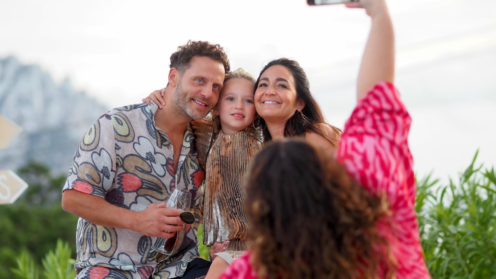 Group posing for a selfie outdoors, smiling and holding drinks at a sunny gathering.
