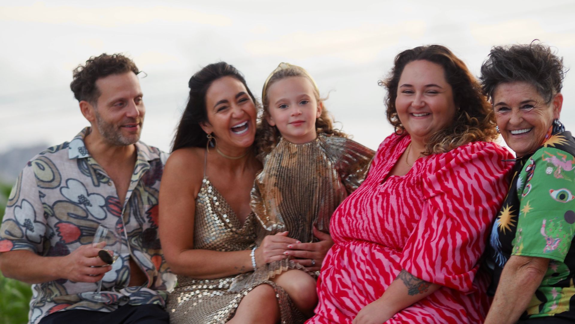 Five people smiling and posing together outdoors at sunset, wearing colorful outfits.