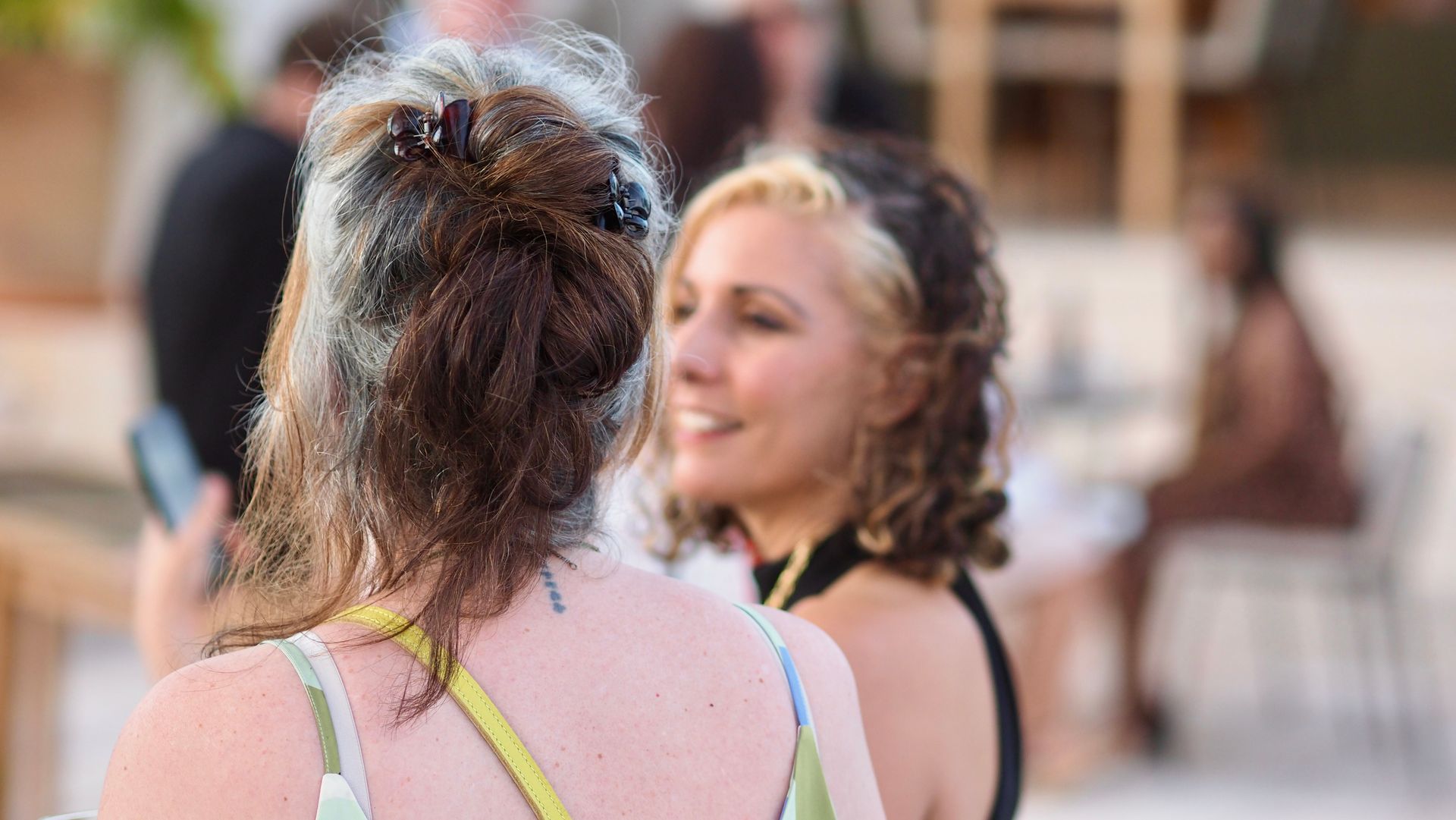 Two women talking outdoors, one facing away with a pink top, the other smiling in a black top.