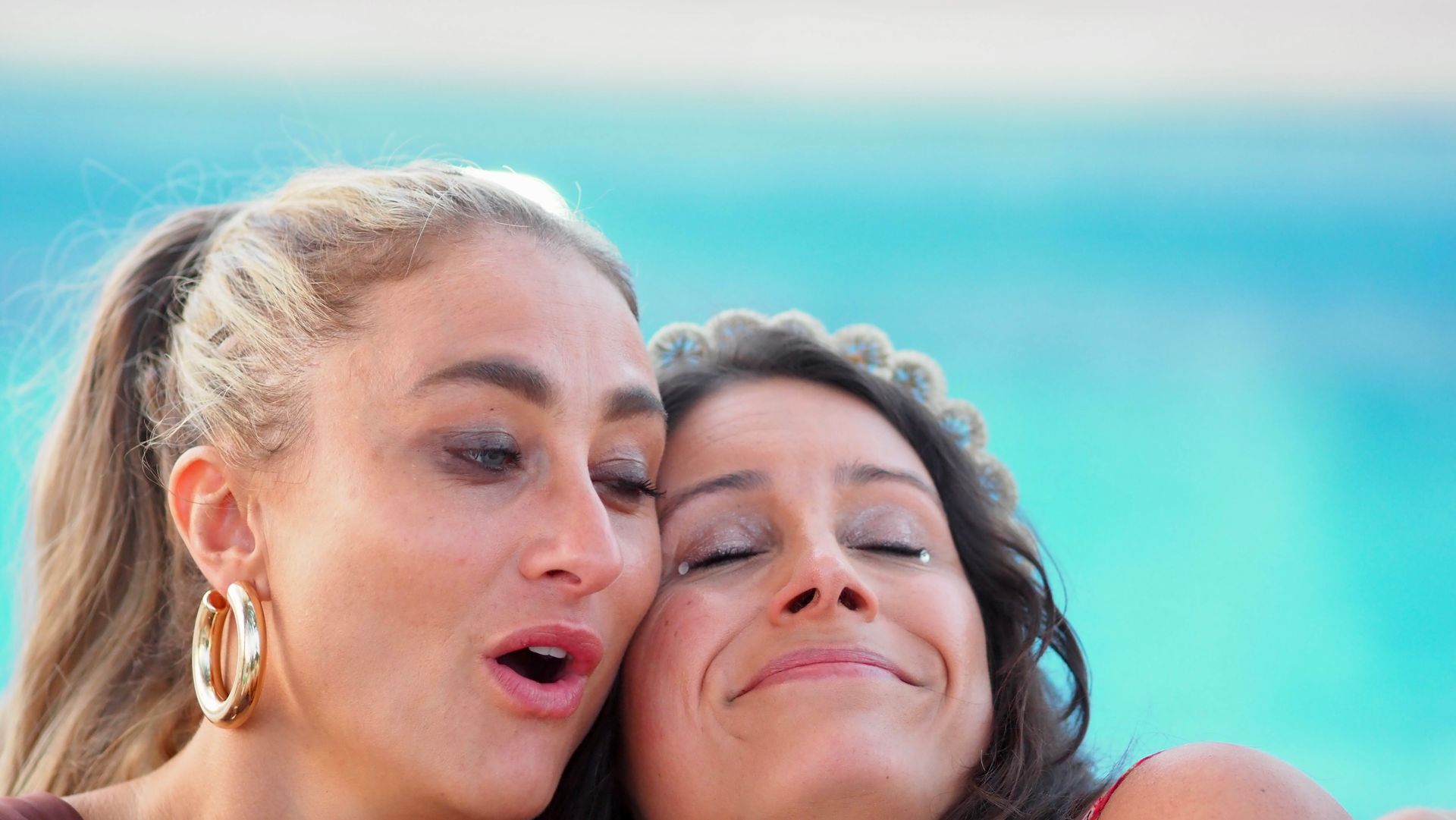 Two smiling friends posing closely at the beach with blue ocean in the background
