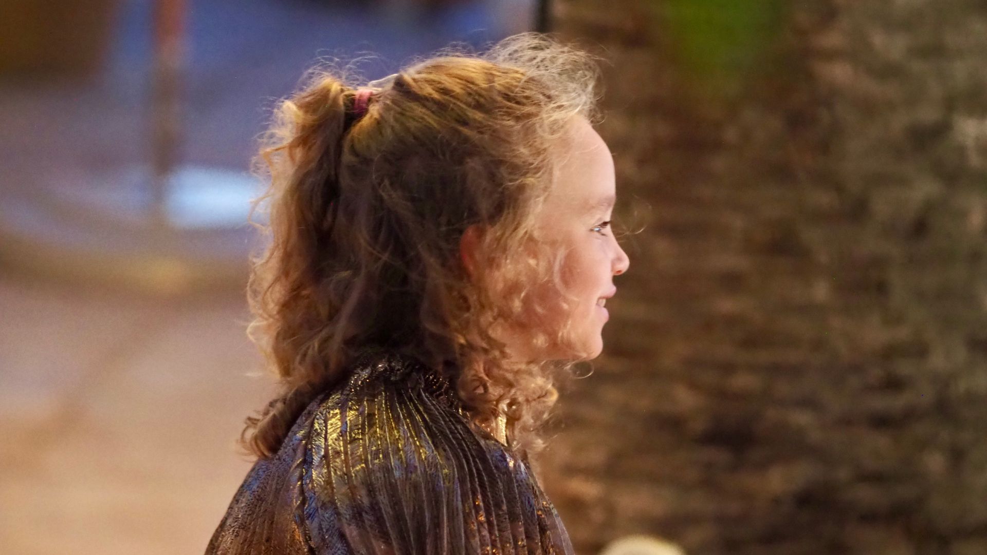 Side-profile of a child with curly hair in a sparkly dress, outdoors in warm evening light