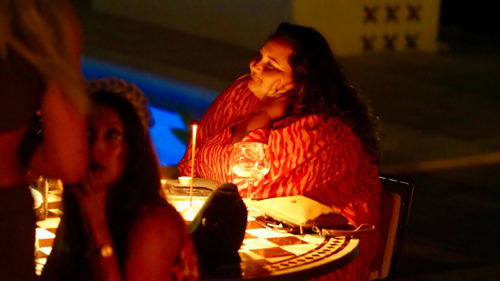 Woman in a red top sitting at a candlelit table, smiling in warm orange light.