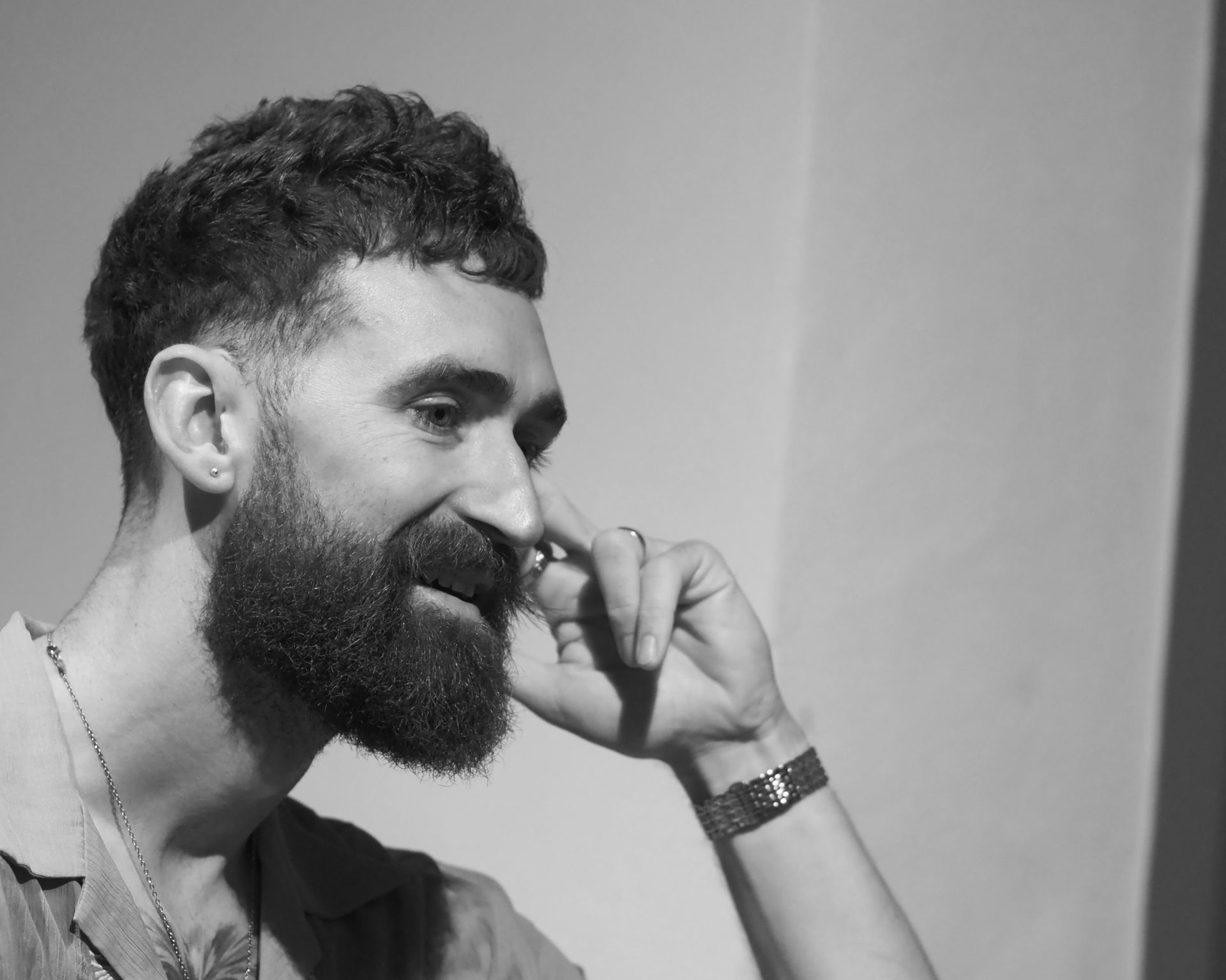 Black-and-white portrait of a smiling bearded man touching his nose with his hand
