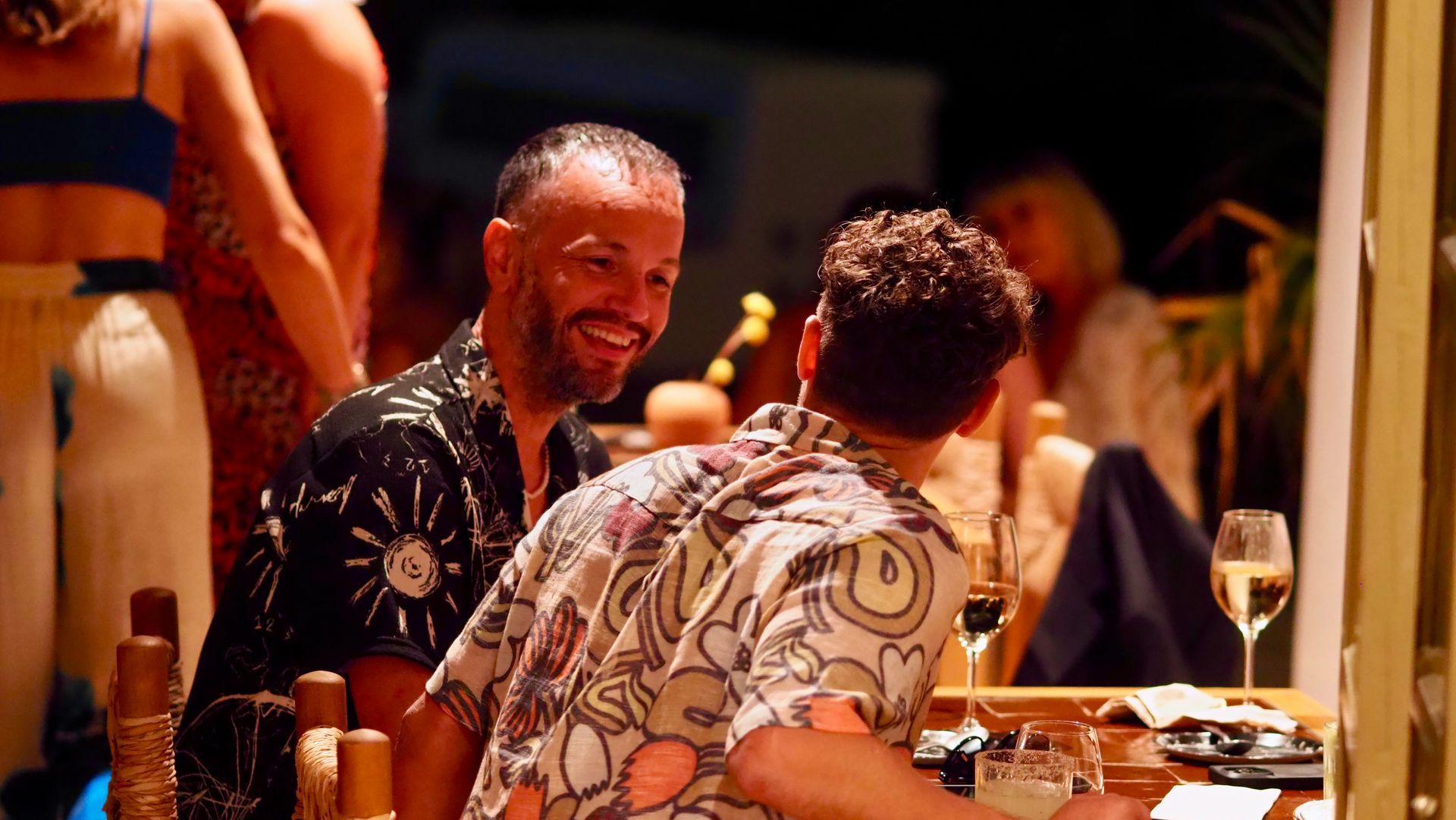 Two people chatting at a candlelit restaurant table, smiling with wine glasses and plates nearby