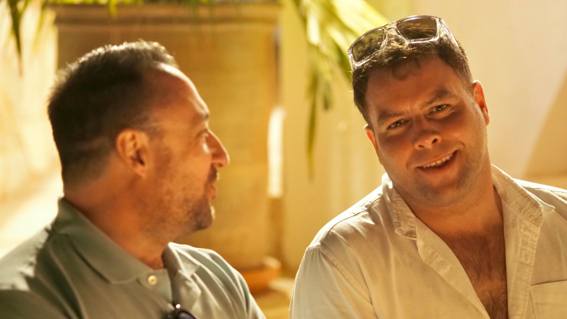 Two people in light shirts smiling and talking in warm sunlight outdoors