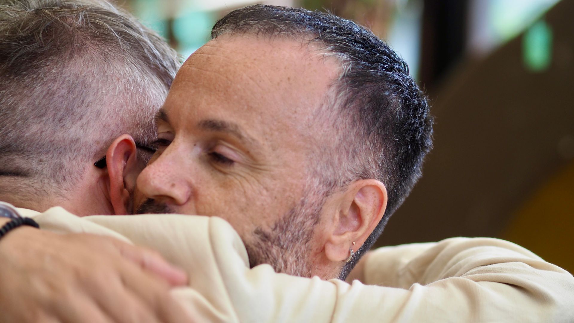 Two people hugging closely in a warm embrace, one with a beard in the foreground.