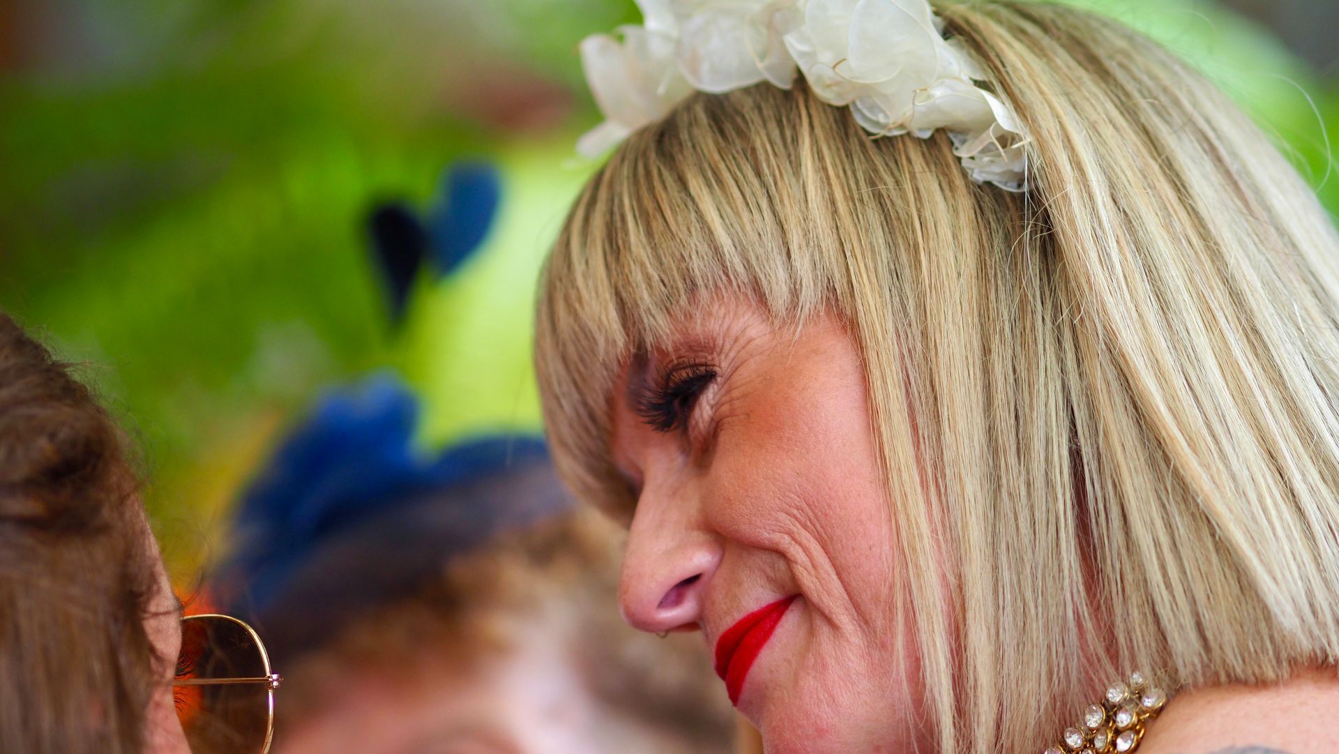 Blonde woman in a white floral headband smiling in profile at an outdoor event