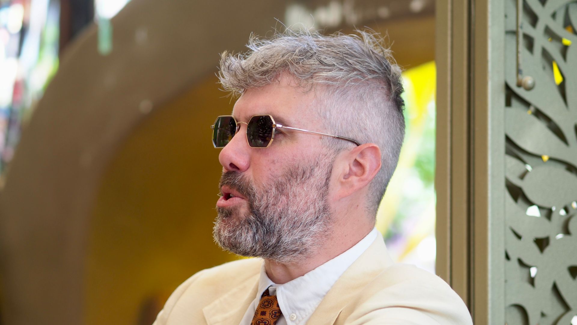 Man in sunglasses and white shirt, seated indoors with a neutral expression