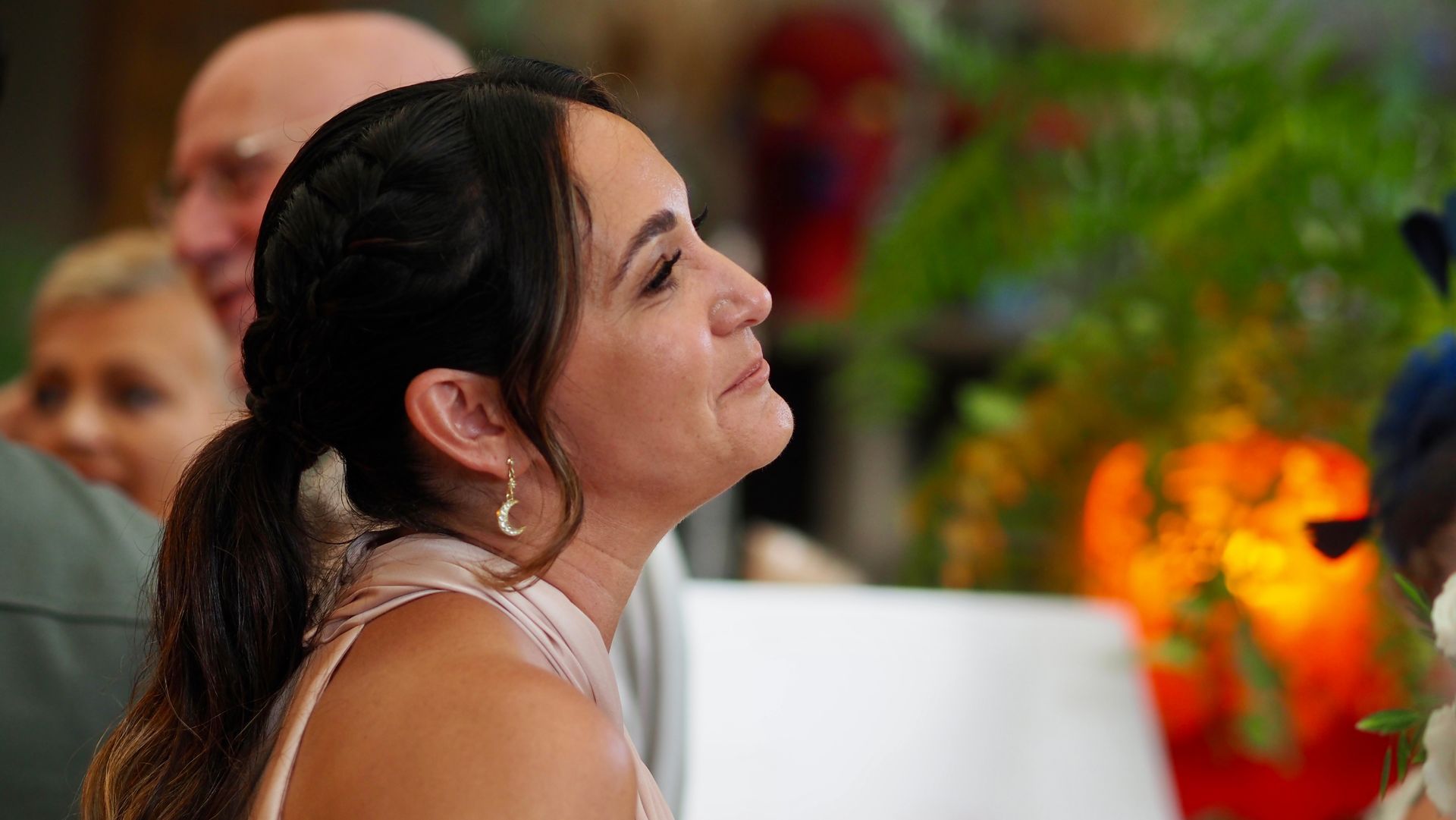 Woman in profile at a formal event, with blurred guests and warm orange lights in the background