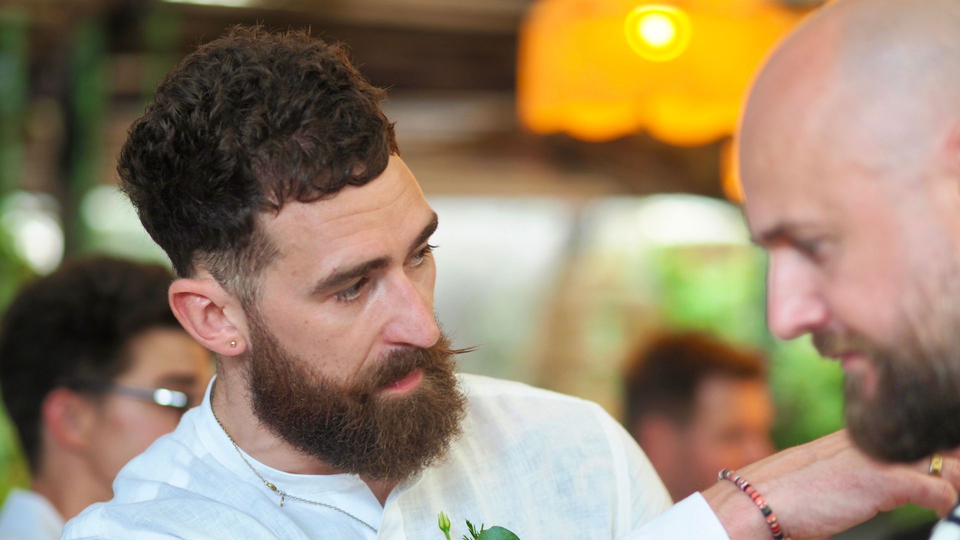 Two bearded men in white shirts talking closely in a warm indoor setting.
