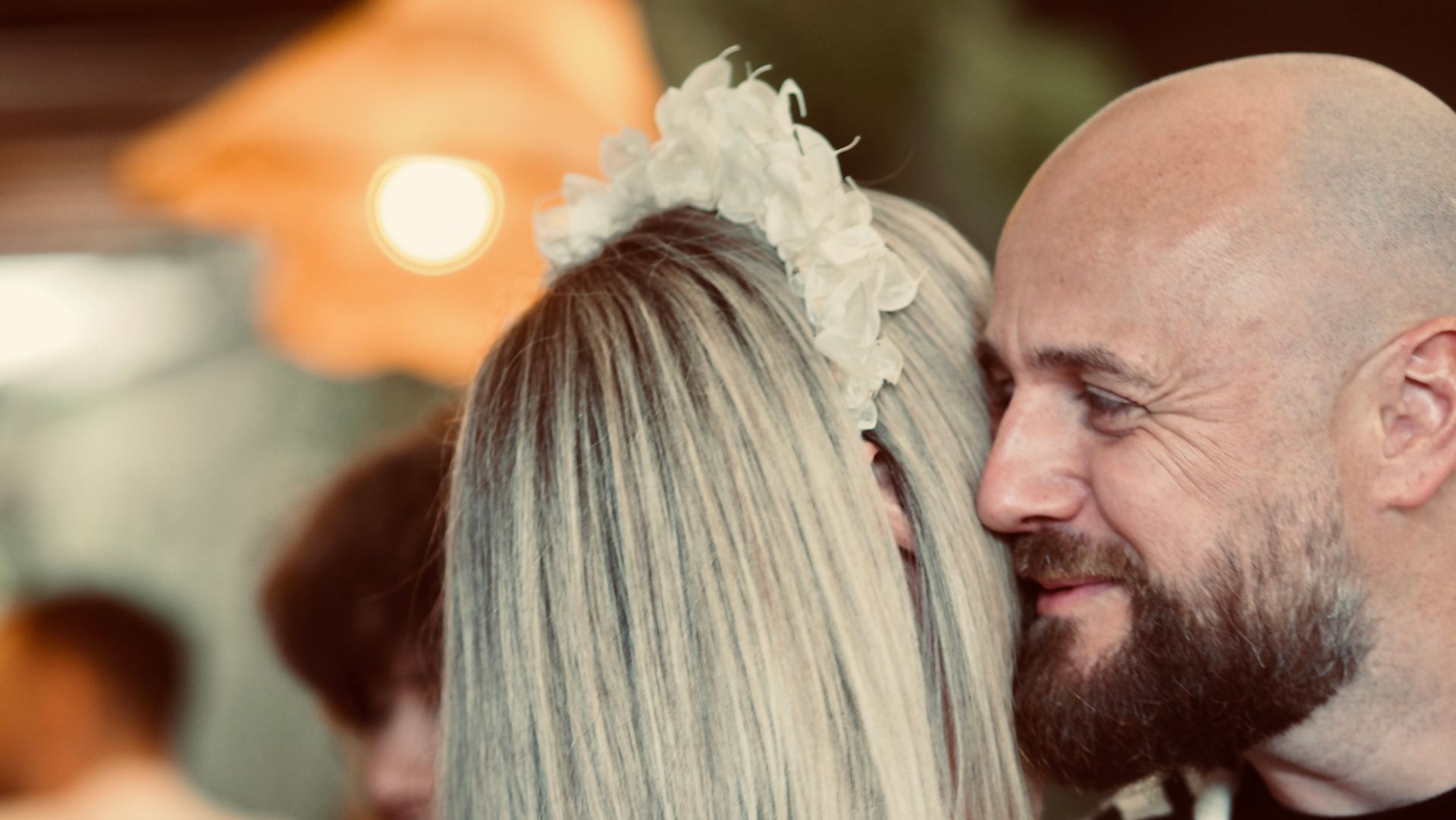 Smiling bald man facing a blonde woman in a softly lit indoor setting