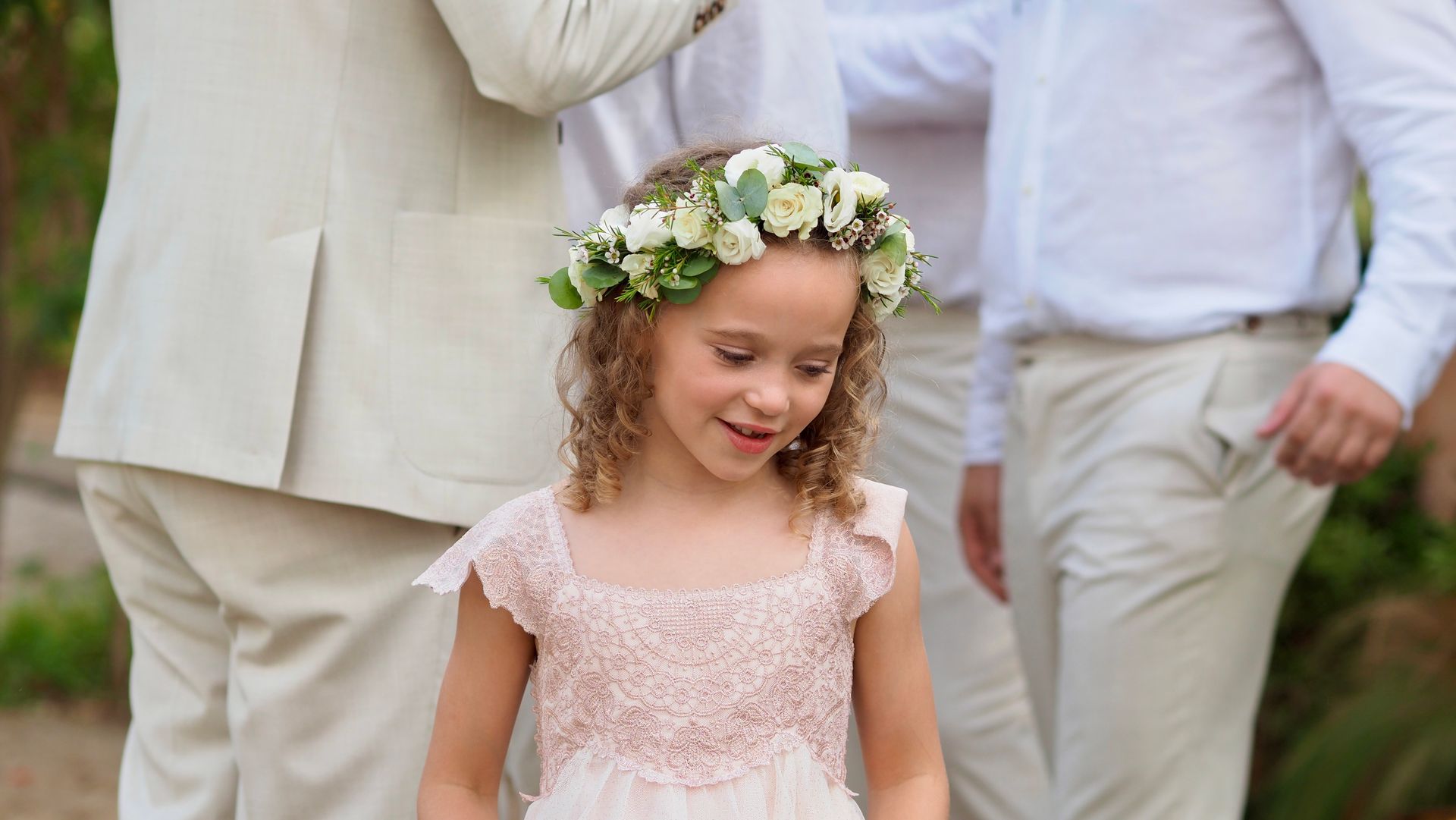 Smiling child wearing a flower crown and pink dress at an outdoor wedding ceremony