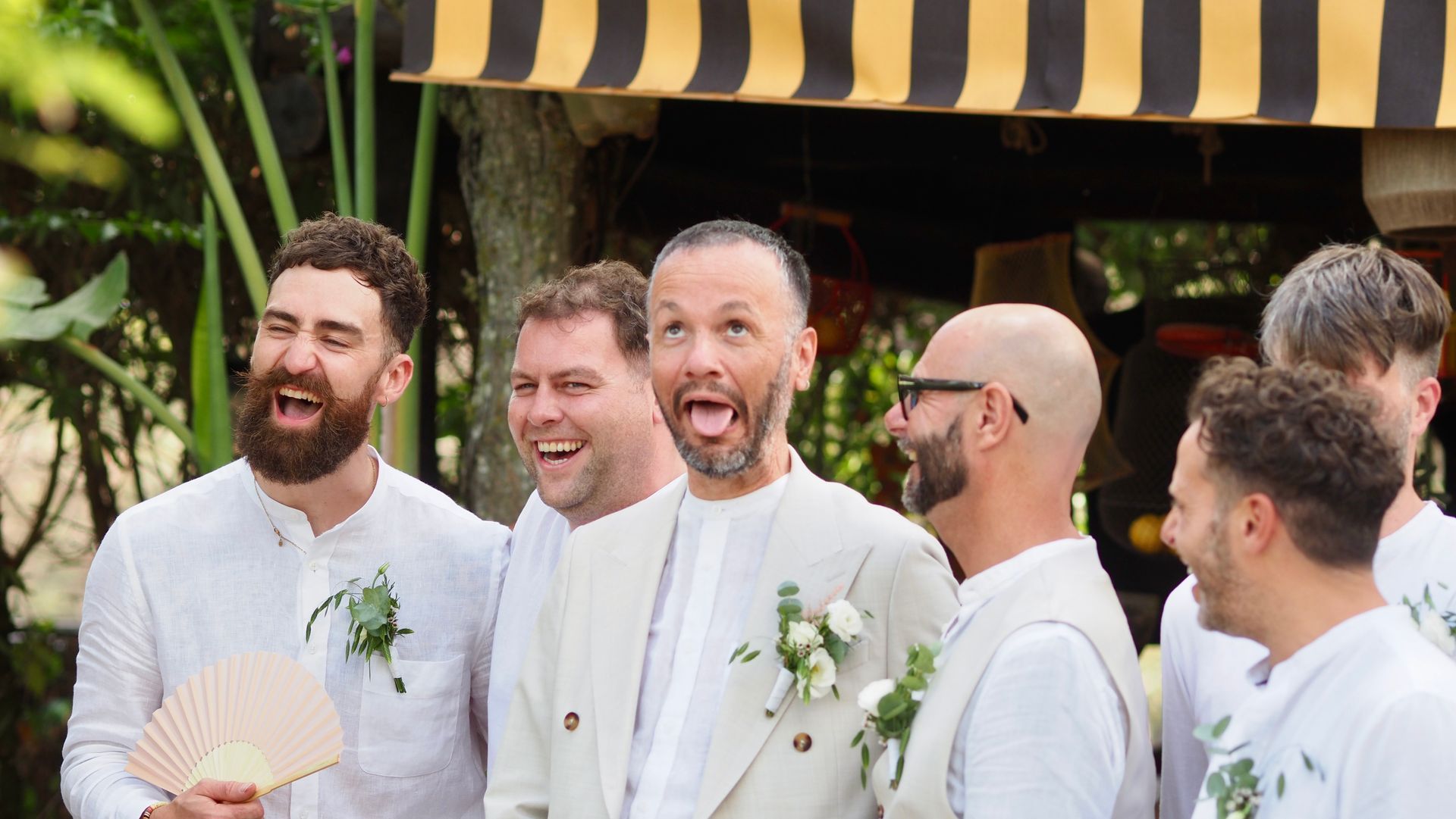Group of men in white suits smiling at an outdoor wedding celebration