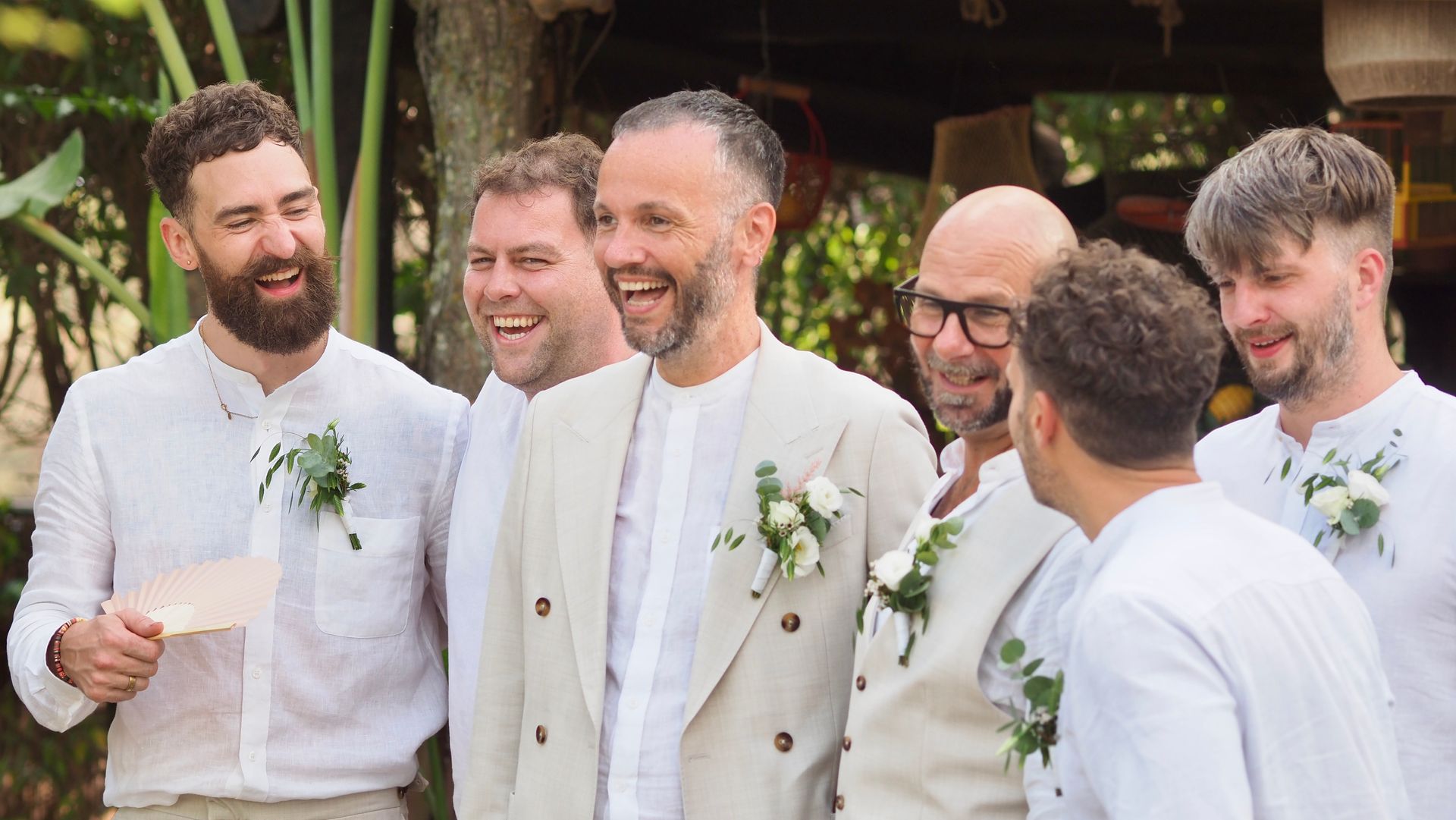 Five smiling people in white outfits chatting outdoors at a celebration