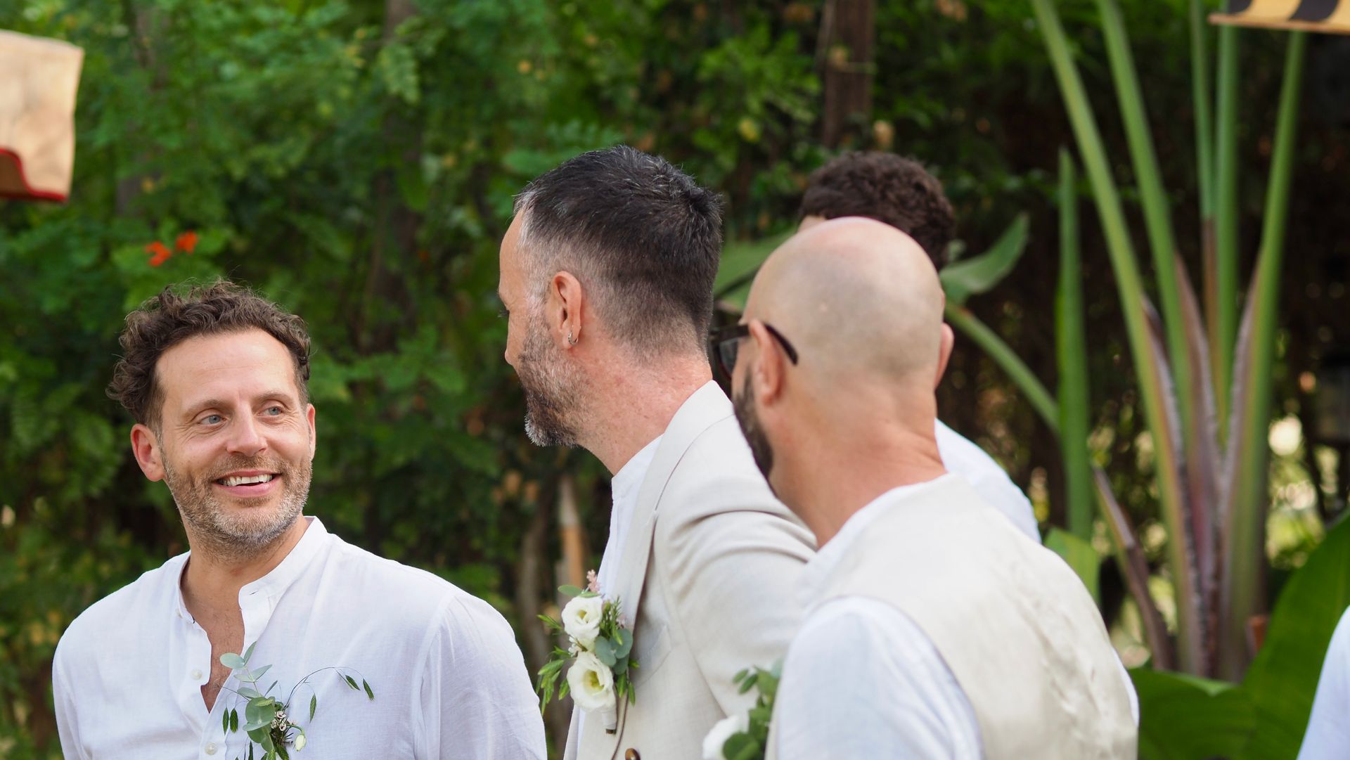 Three men in white shirts smiling and talking outdoors at a garden event