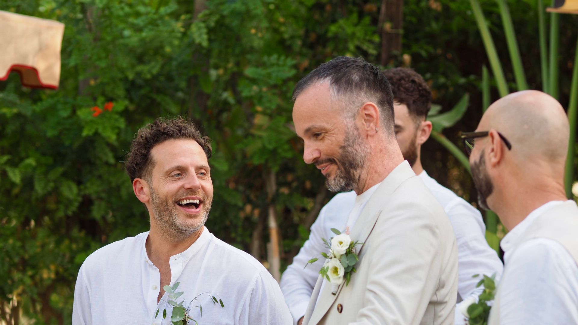 Three men in white shirts smiling outdoors at a wedding-like gathering