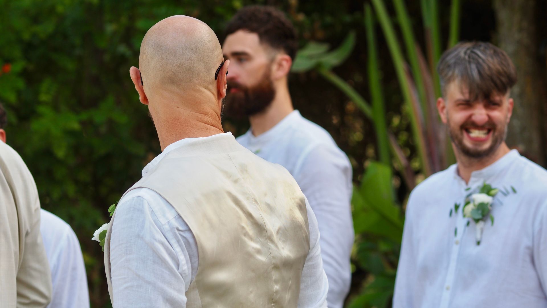 People in white shirts and vests chatting outdoors at a garden event, one smiling.