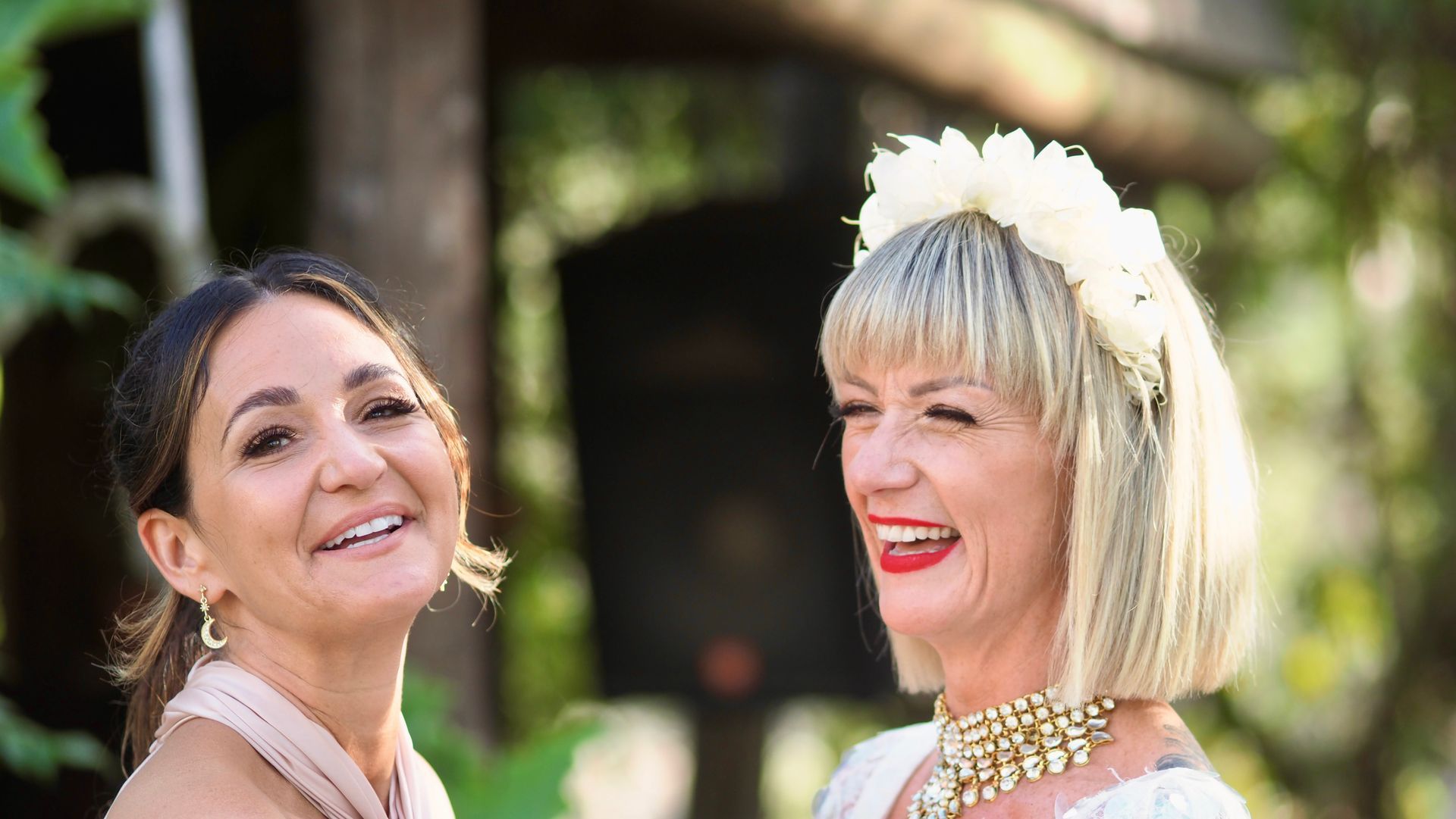 Two smiling women outdoors, one with a white floral headpiece and blonde bob haircut.