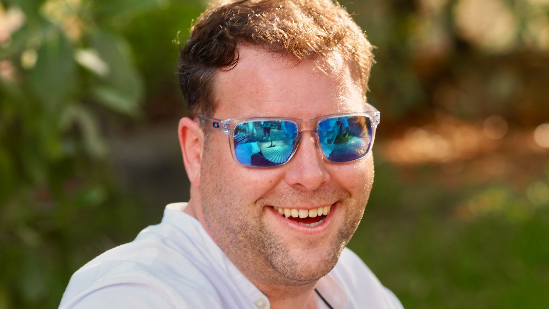 Smiling person wearing blue mirrored sunglasses outdoors in sunlight