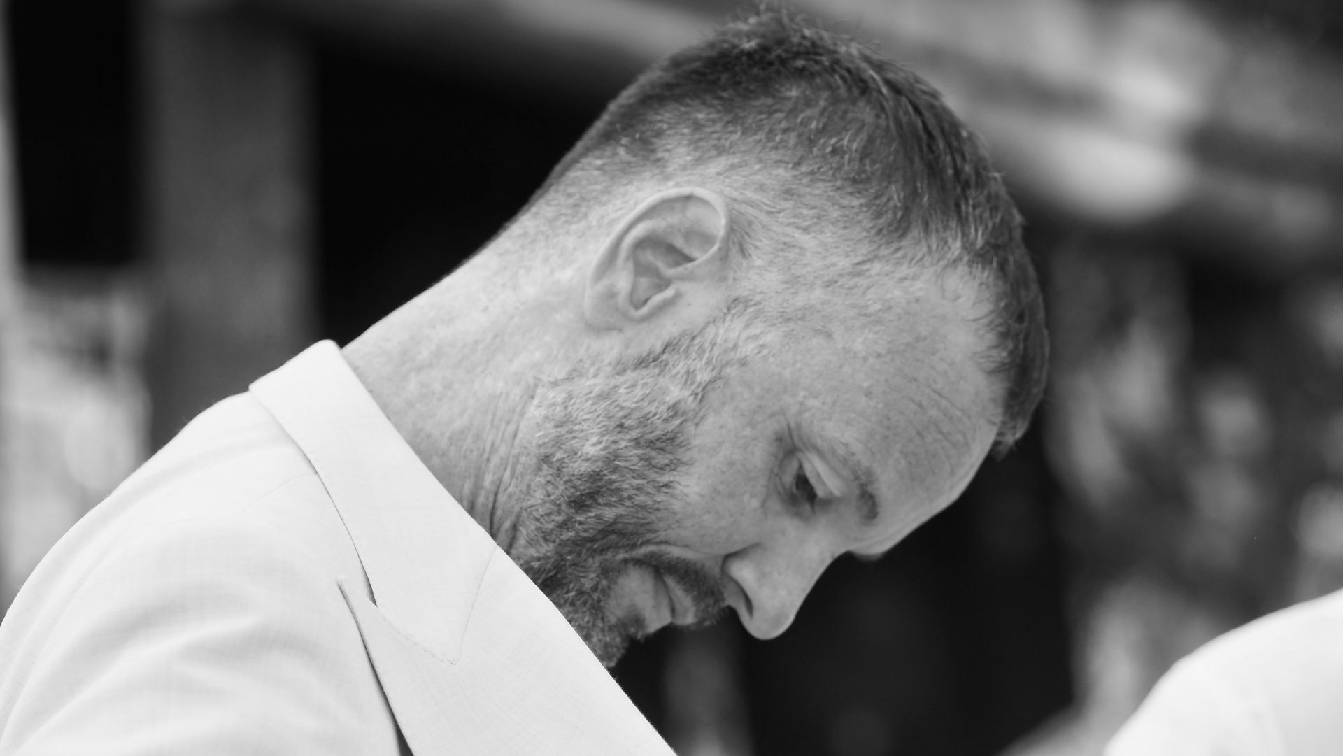 Man in a white shirt looking down, head bowed in a black-and-white close-up