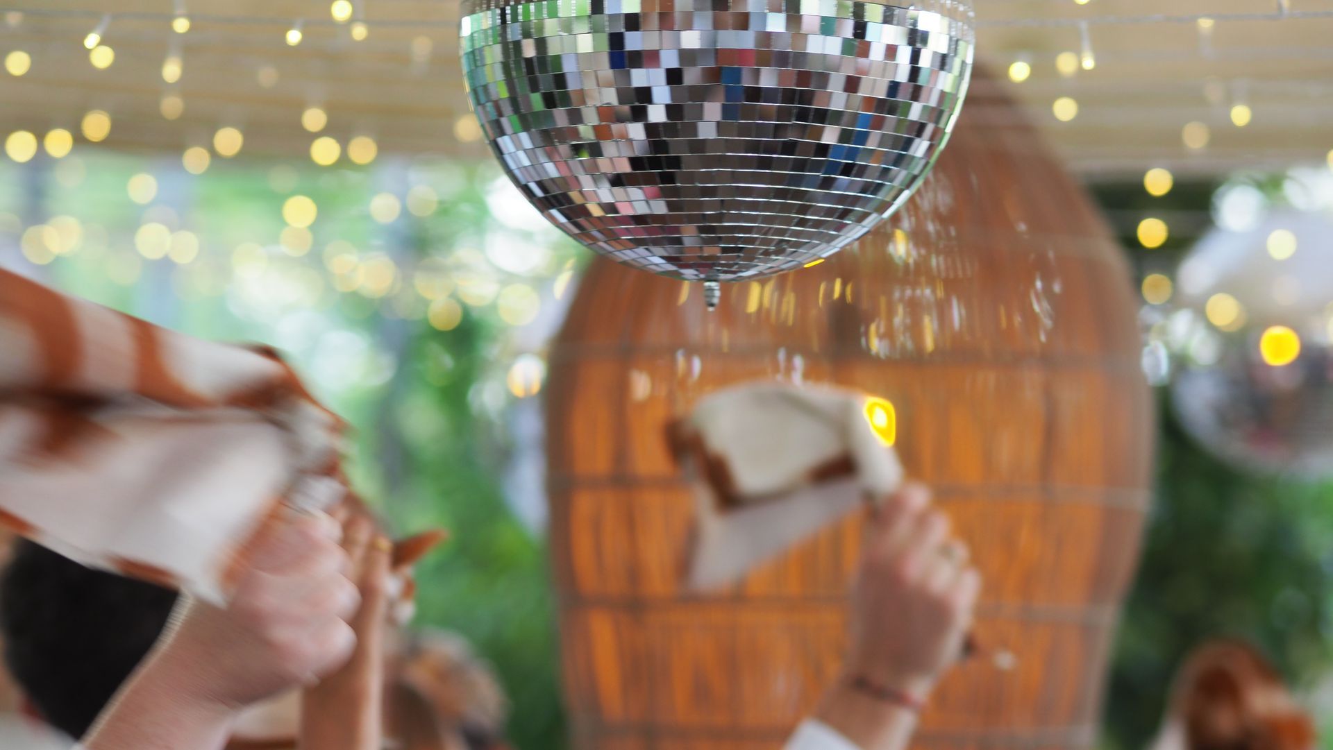 Disco ball hanging above a festive outdoor celebration with blurred string lights and wooden decor