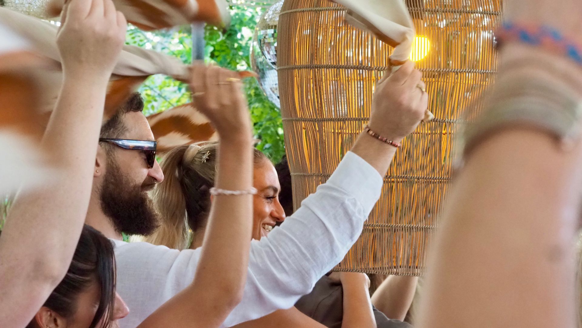 People raising hands and clapping at an outdoor celebration with gold decorations