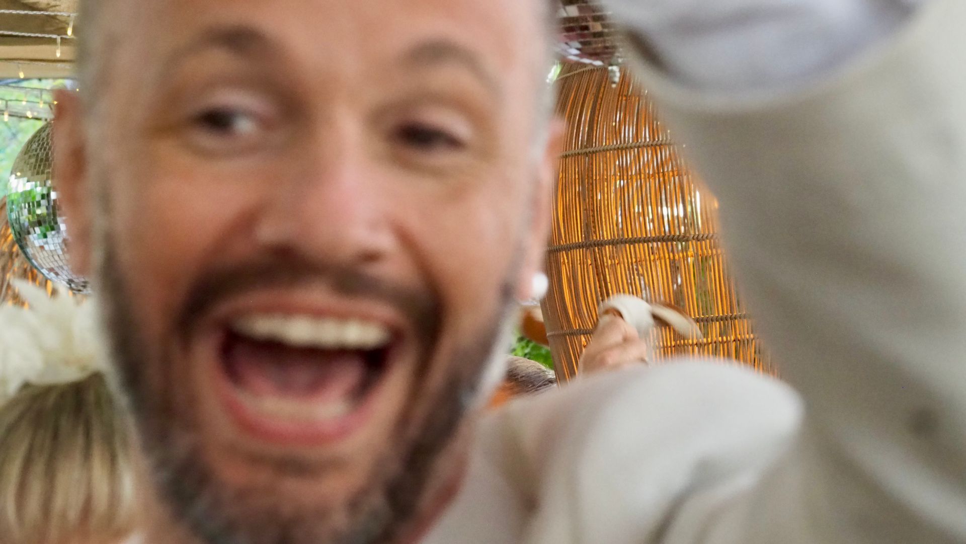 Smiling man close-up with open mouth and raised arm in a bright indoor setting