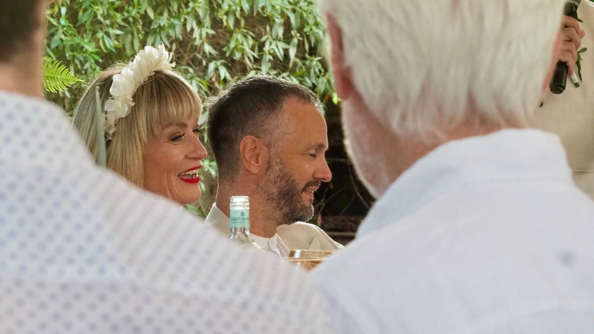 Smiling people seated outdoors at a social gathering, with white and floral clothing in the foreground