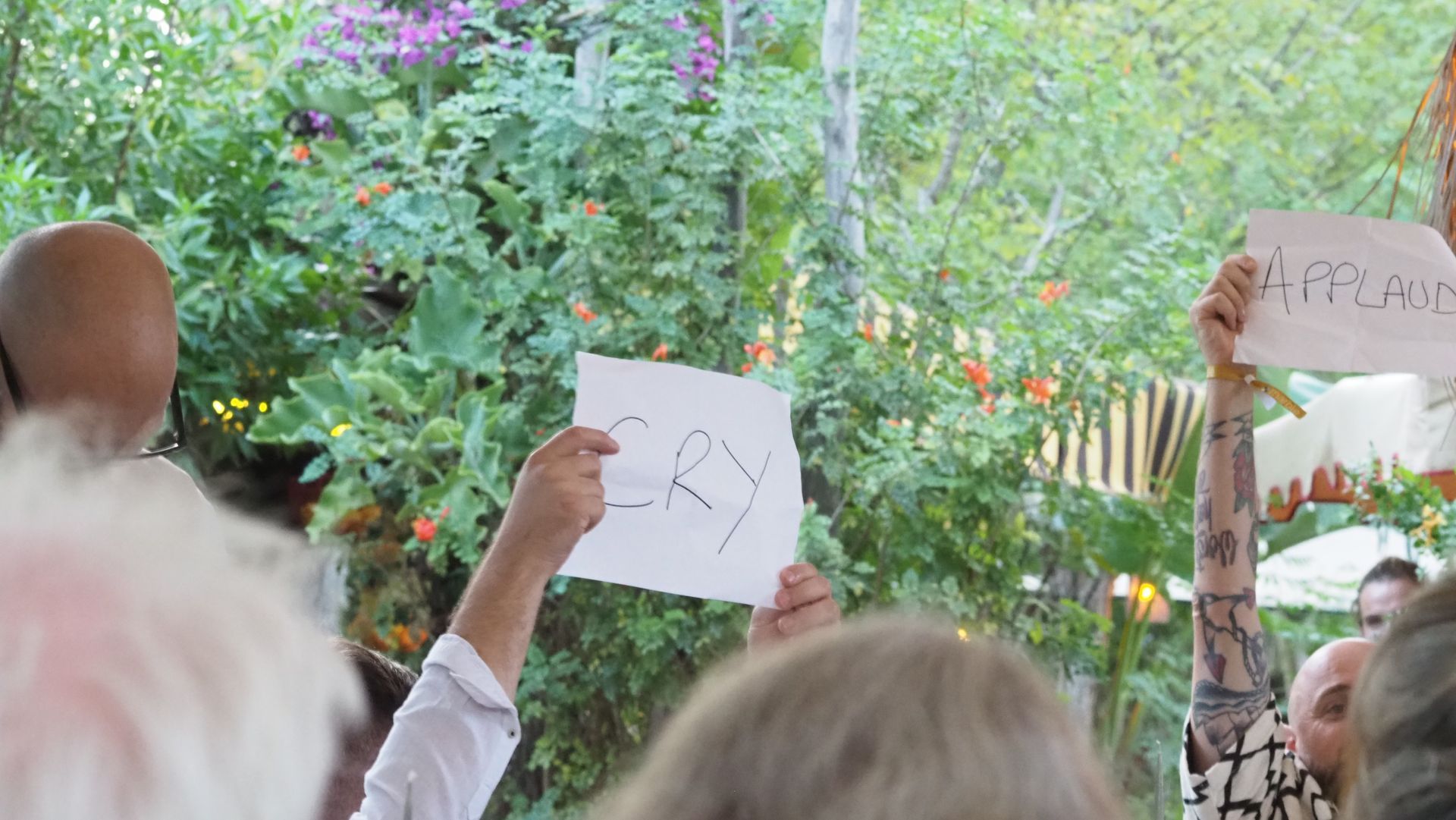 People holding handwritten protest signs in a leafy outdoor crowd