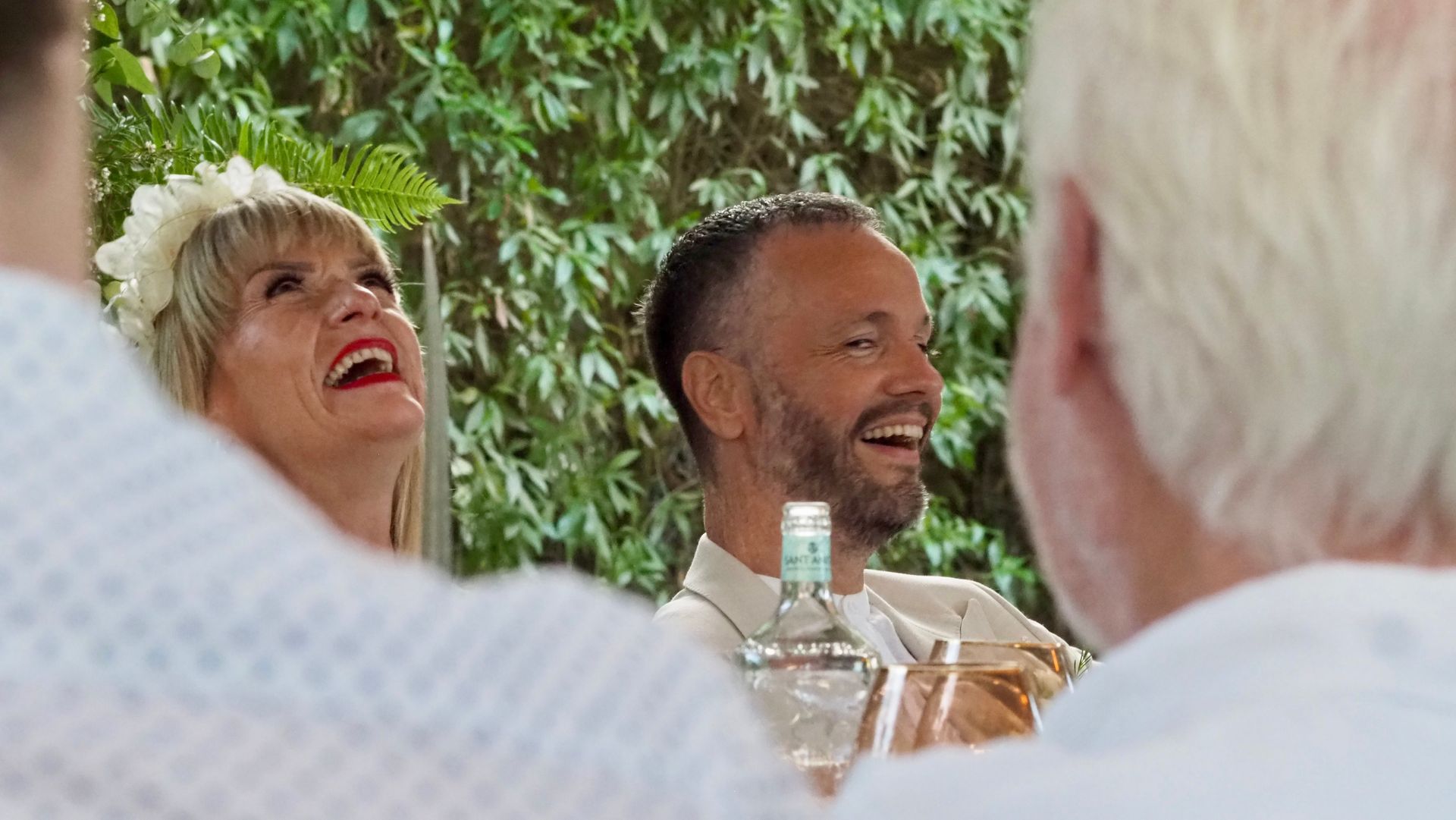 People laughing at a table outdoors with green foliage in the background