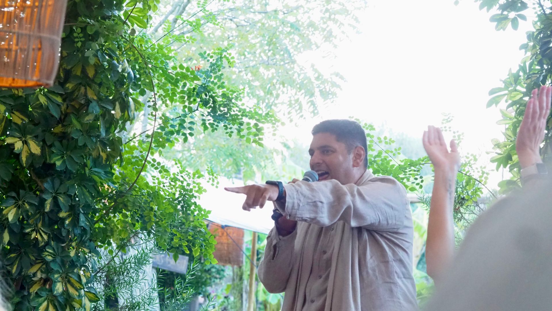 Man pointing and smiling in a lush outdoor garden with bright sunlight and greenery