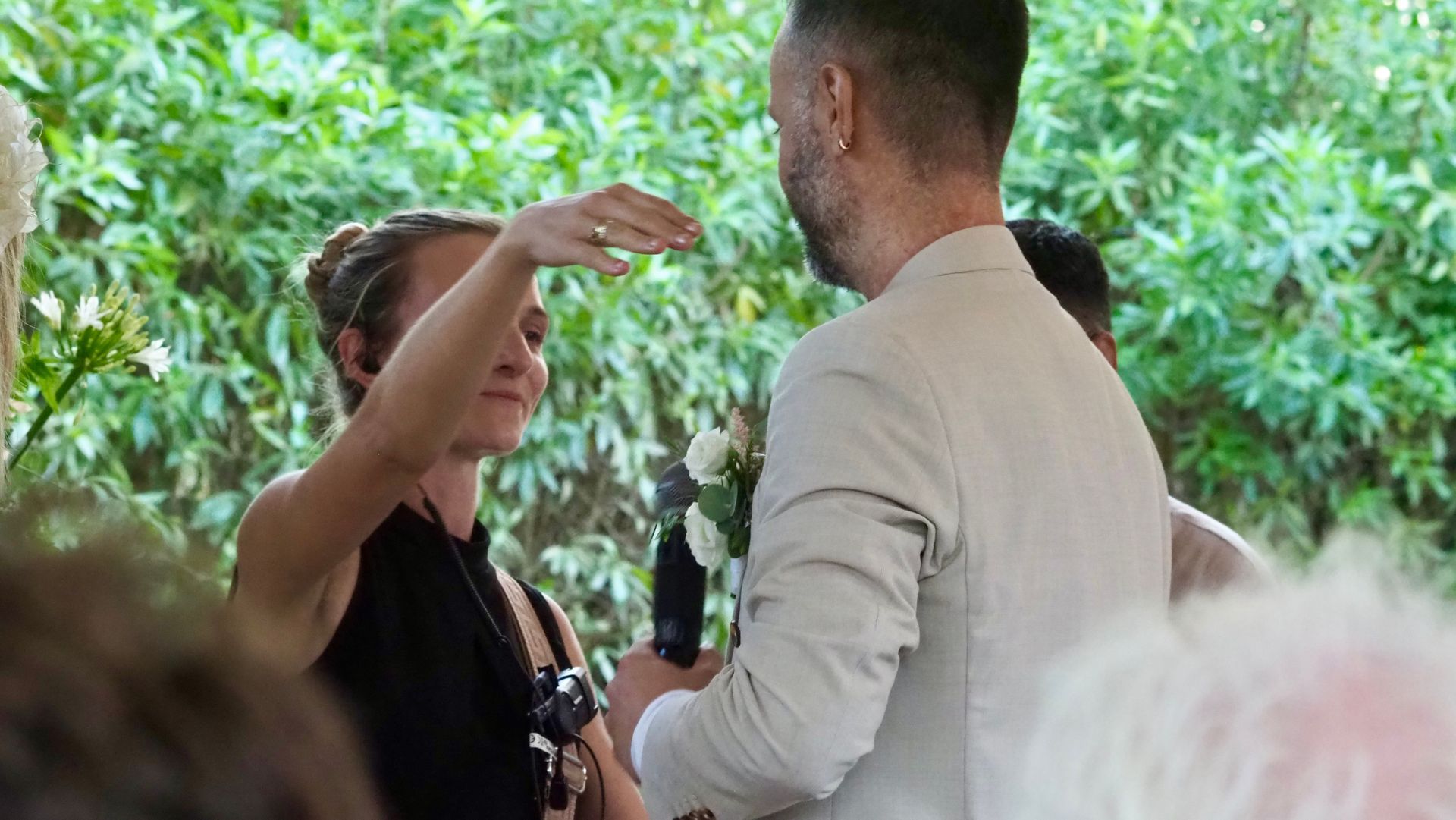 Two people talking outdoors in a leafy setting, one gesturing while facing the other.
