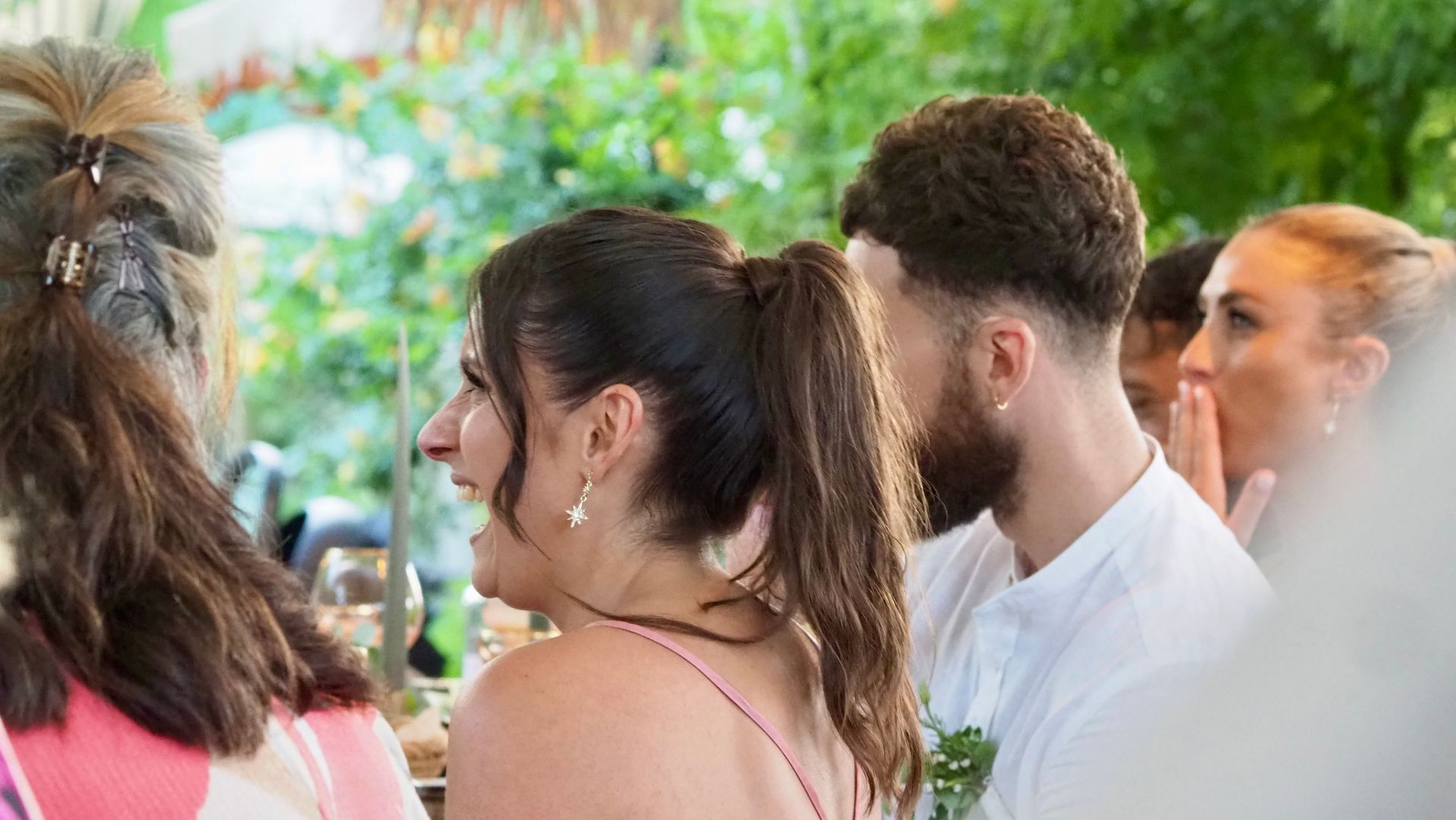 People seated at an outdoor event, viewed from behind, with floral decor in the background.