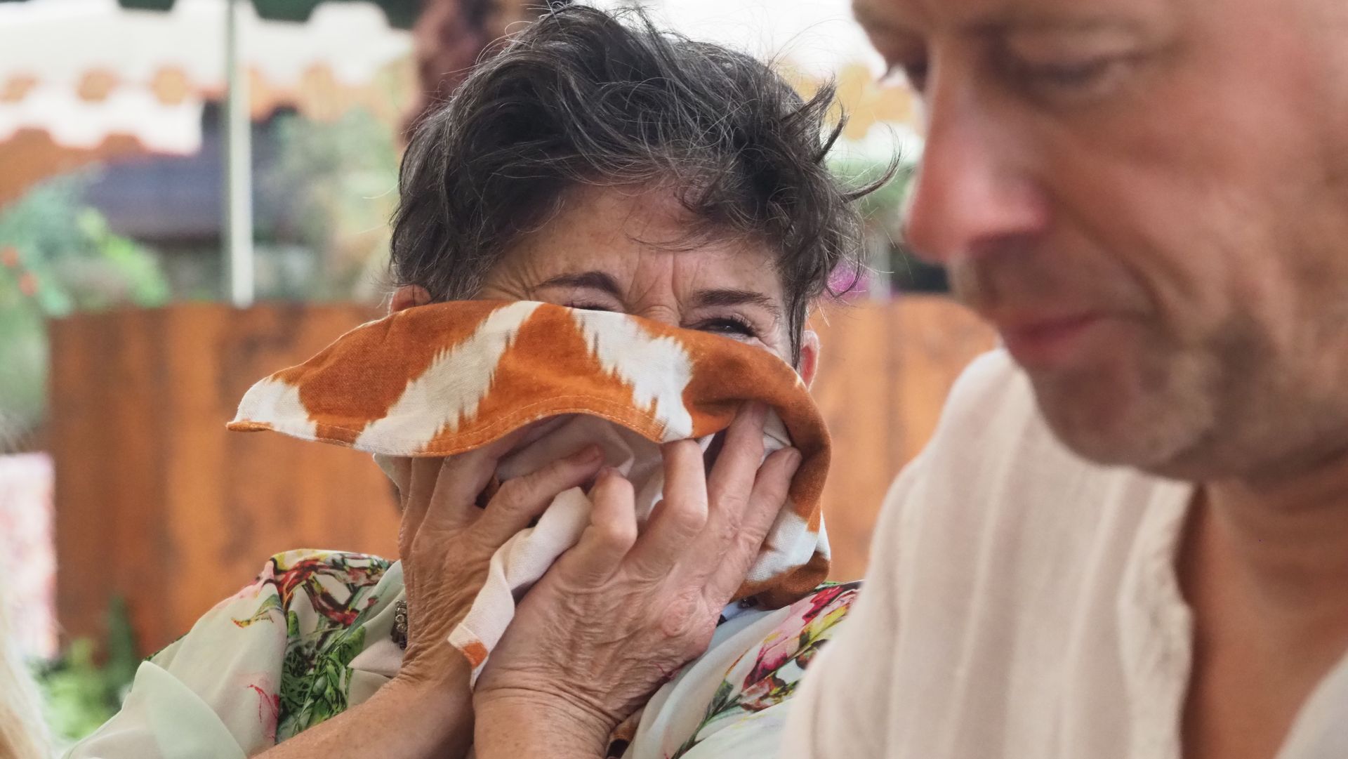 Person smelling a large orange-and-white mushroom at an outdoor market stall