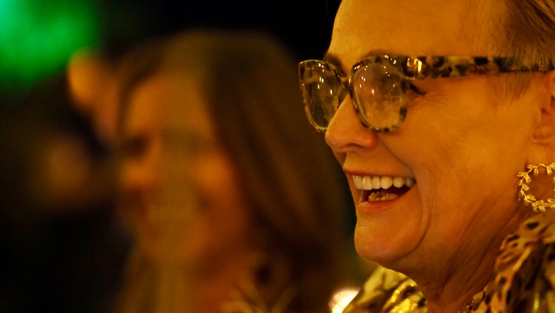 Smiling woman in glasses and leopard-print earrings at a warmly lit event