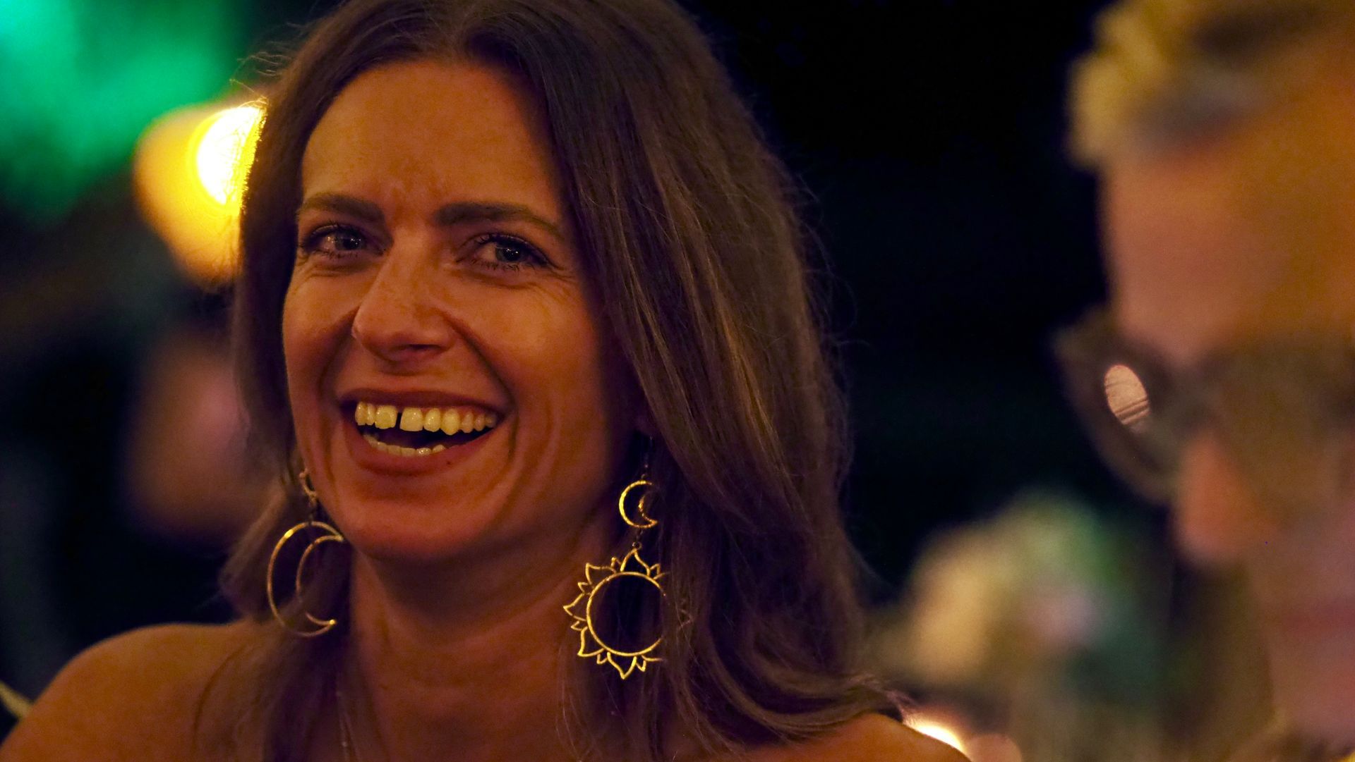 Smiling woman with large hoop earrings in warm, dimly lit social setting