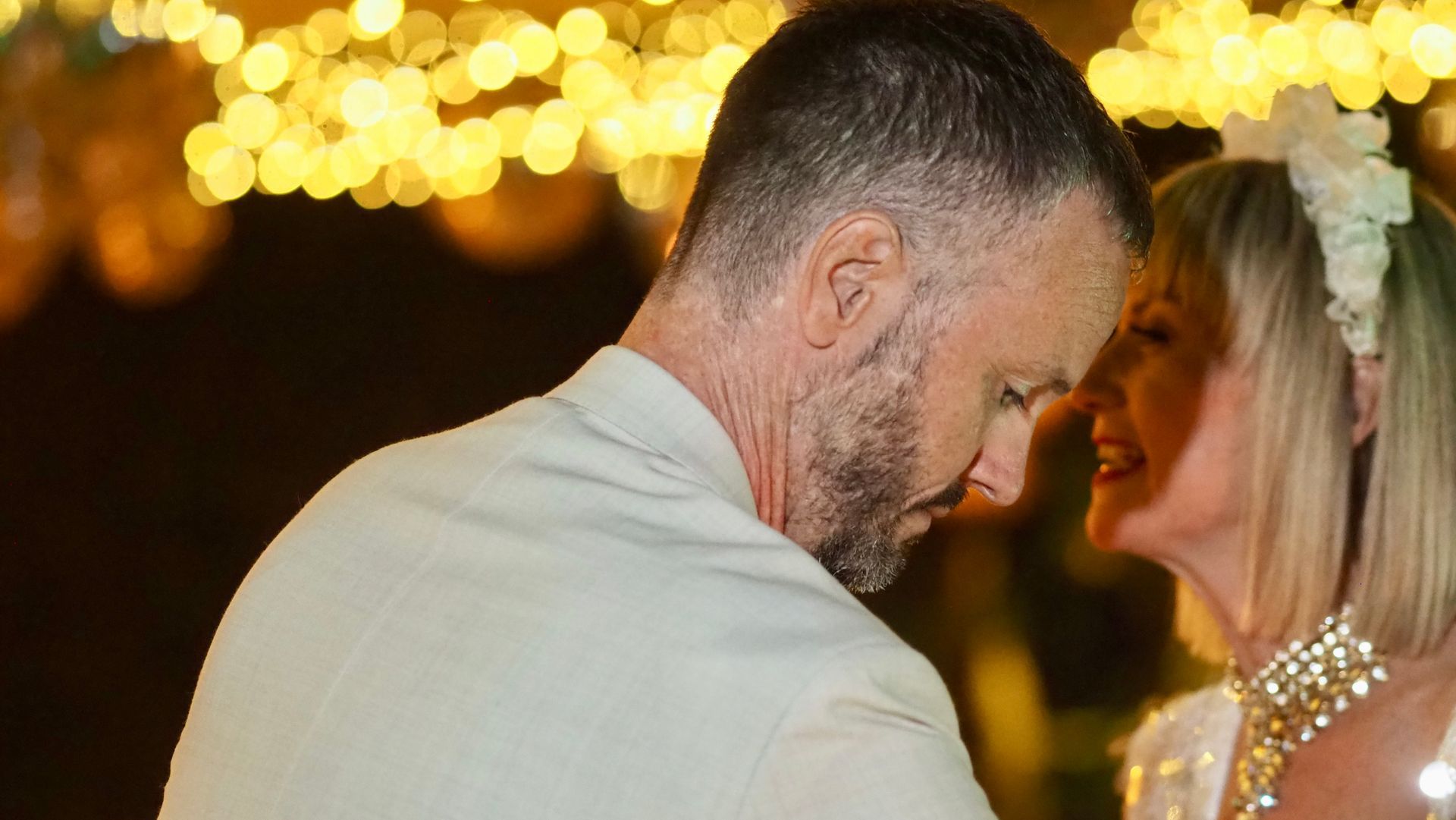 Couple leaning forehead to forehead at a warmly lit wedding reception with golden bokeh lights