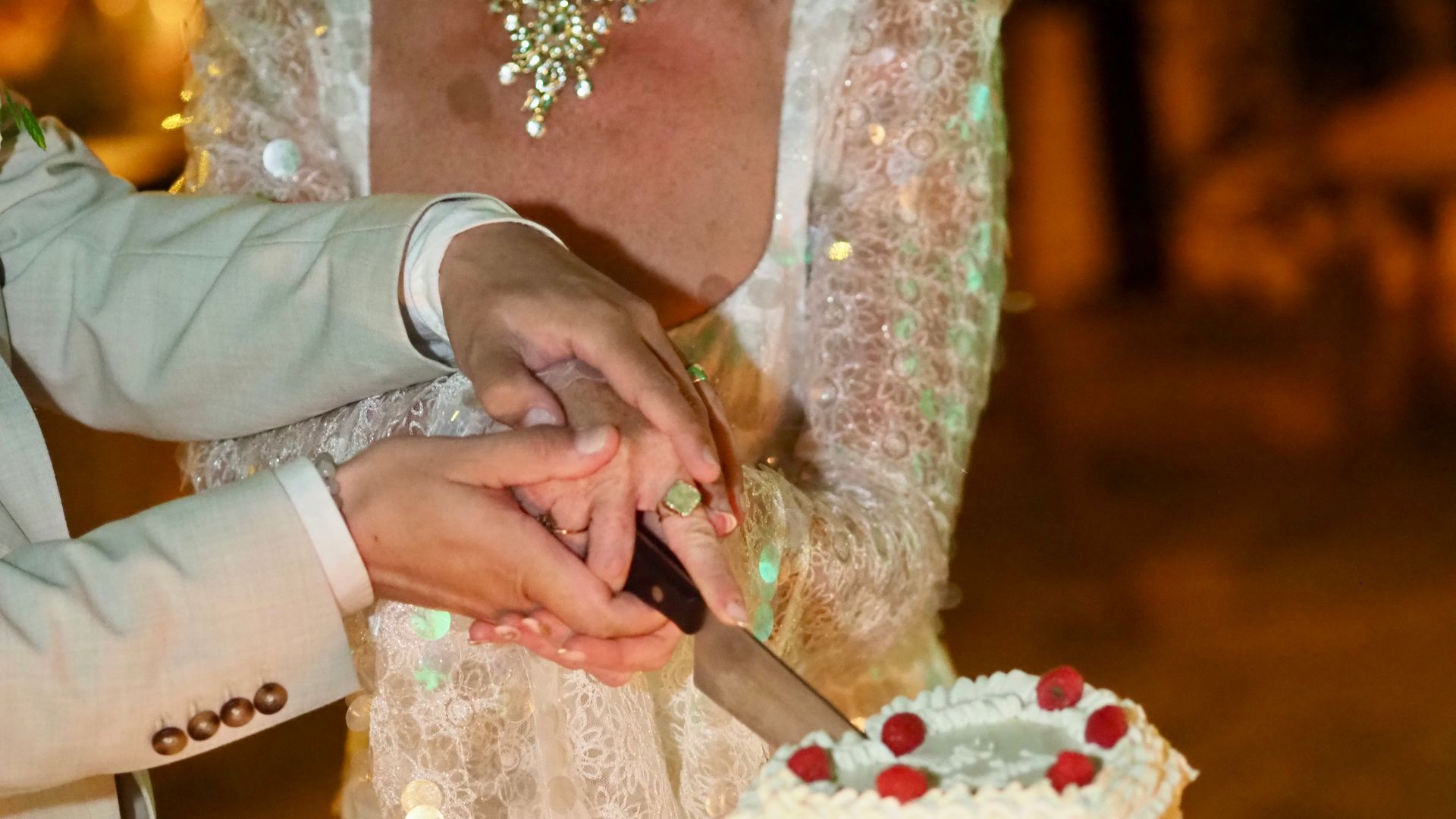 Hands cutting a small white cake topped with red cherries at a formal celebration