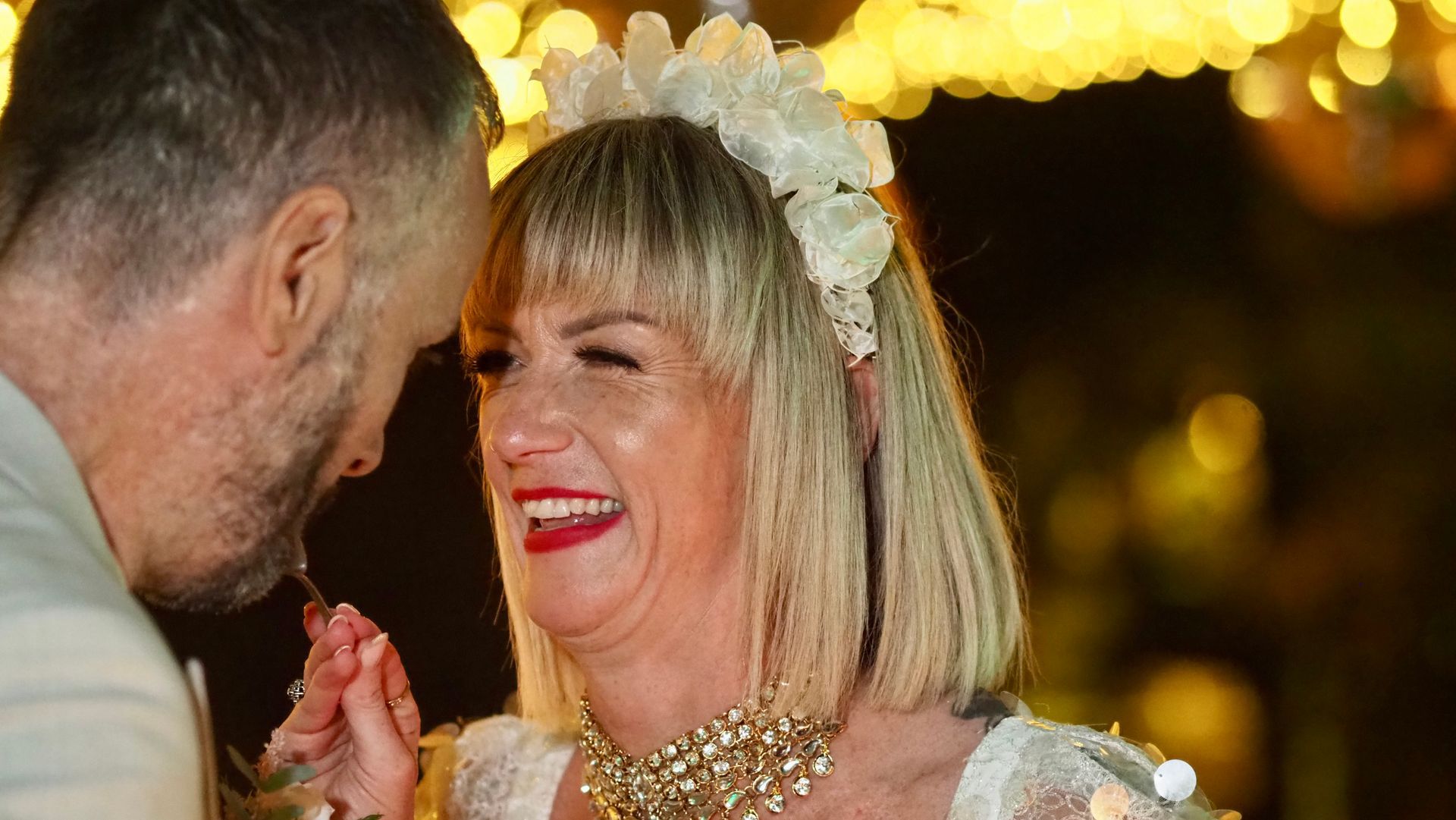 Two people laughing and clapping at a festive event, with warm lights in the background.