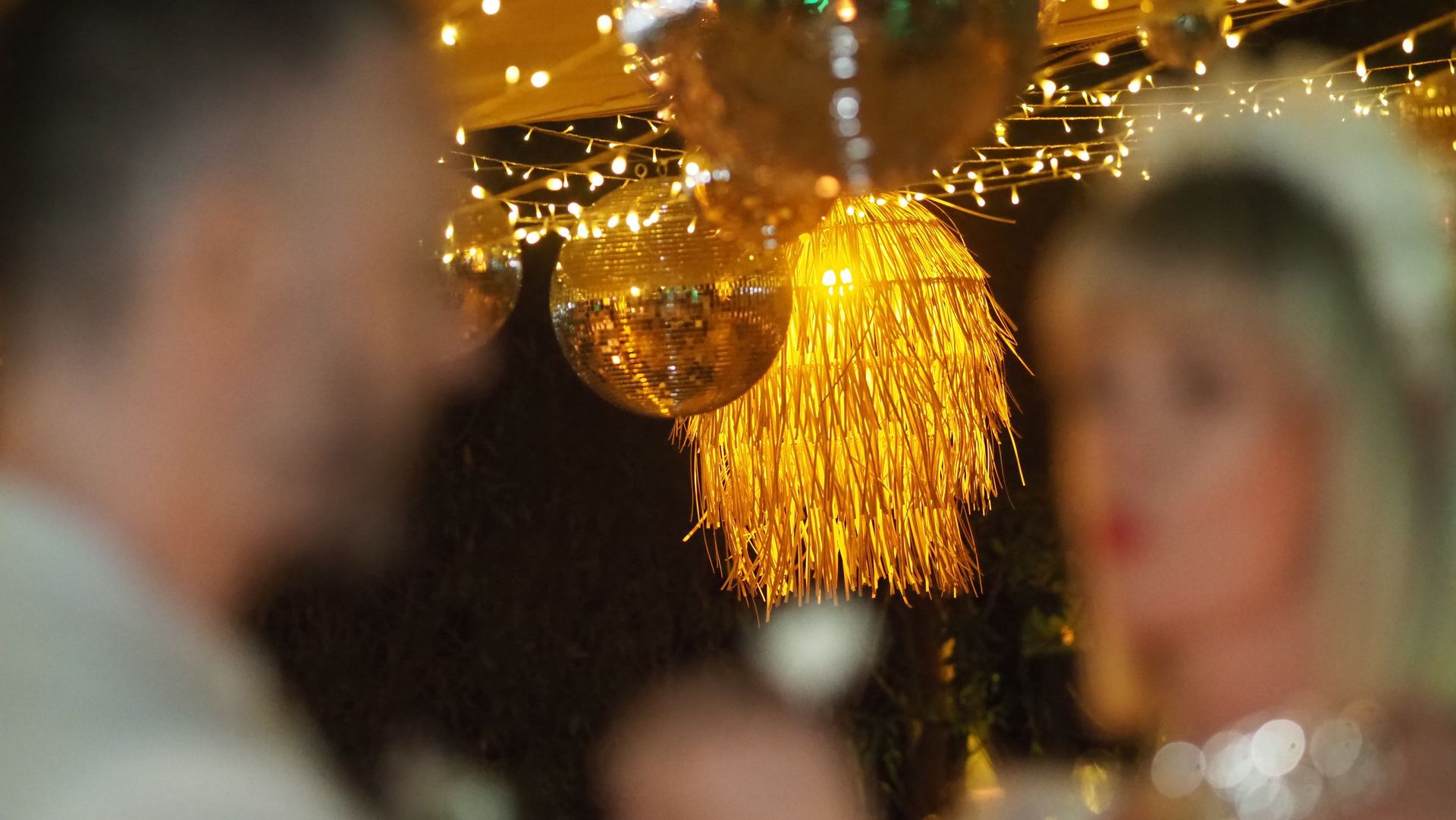 Golden tassel chandelier centered in a dim, blurred party scene with people in the background
