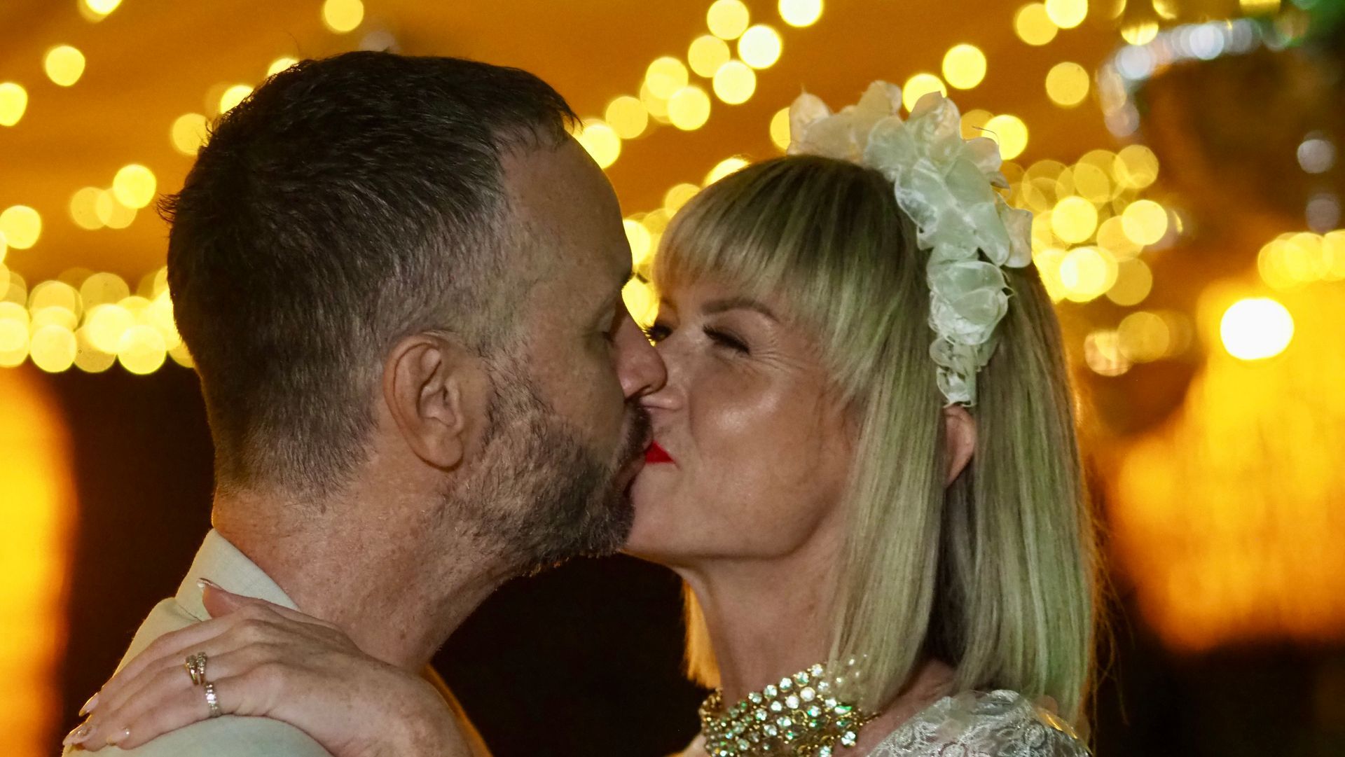 Close-up of a couple kissing at a warmly lit event with golden bokeh lights in the background
